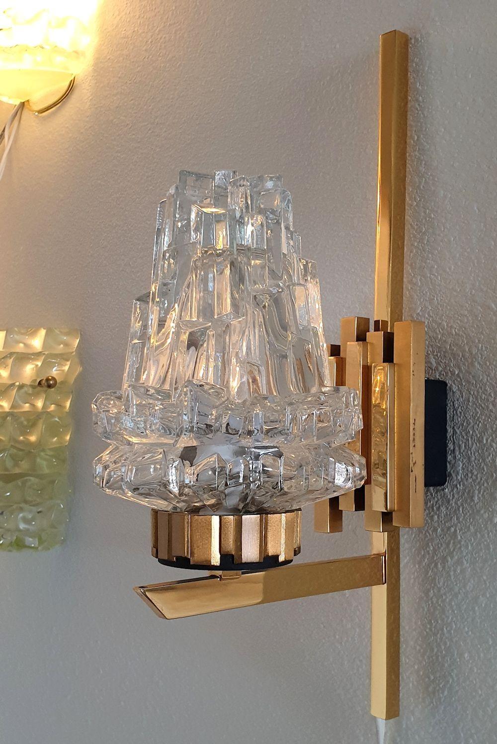 Mid-Century Modern pair of stylish sconces, by Maison Arlus, France 1950s.
The vintage pair of sconces is made of a sculpted thick clear crystal shade, nesting the light, and a brass frame with black accents.
1 Light each, rewired for the US.
In