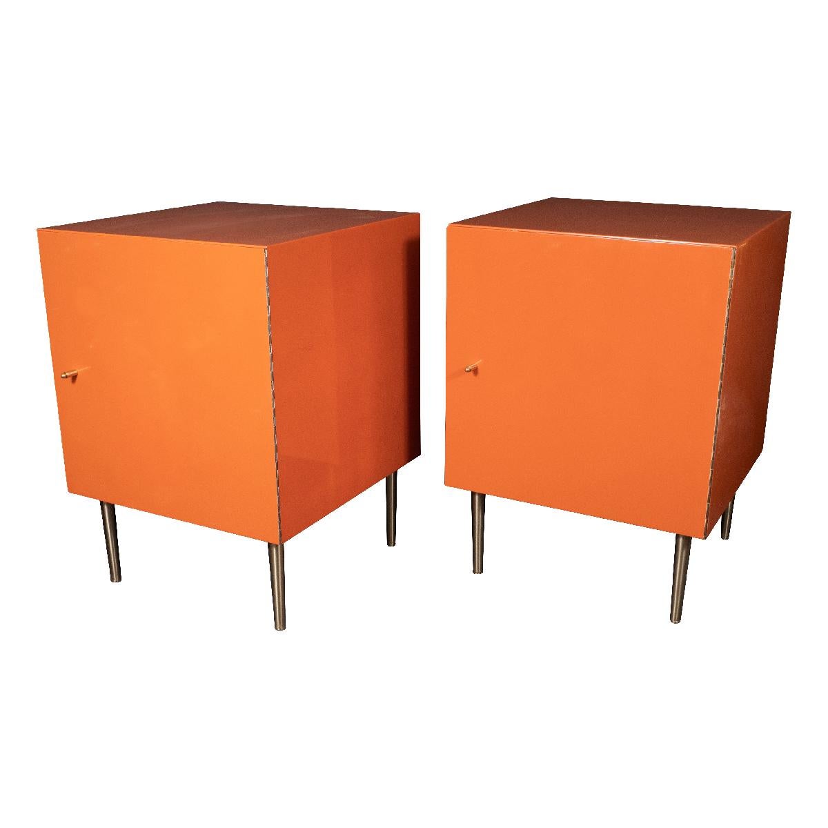 Pair of orange, painted wood cabinets with brass pulls, tapered brass legs and mirrored interiors. Some minor chips in paint finish on face and near hinge.