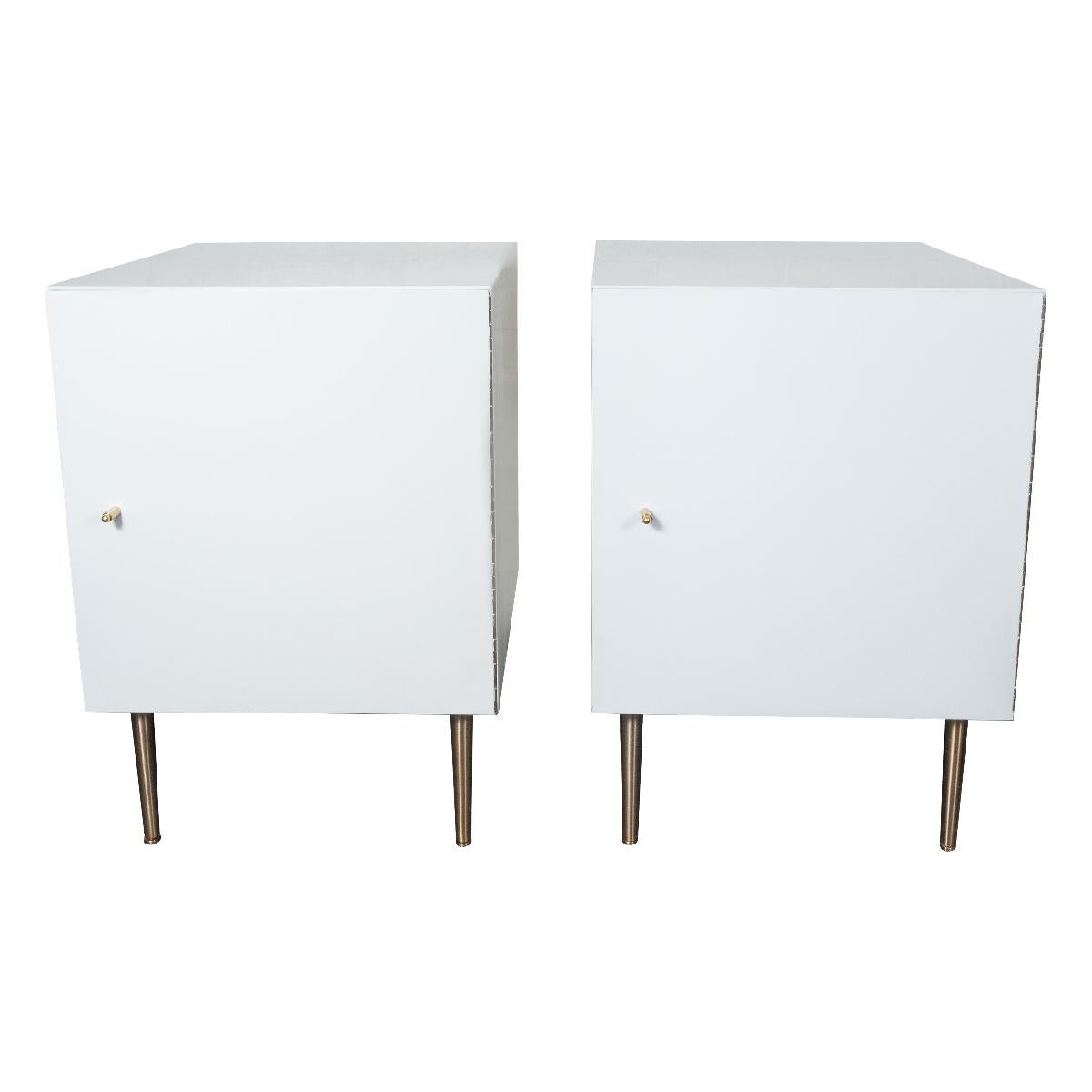 Pair of white, painted wood cabinets with brass pulls, tapered brass legs and mirrored interiors.