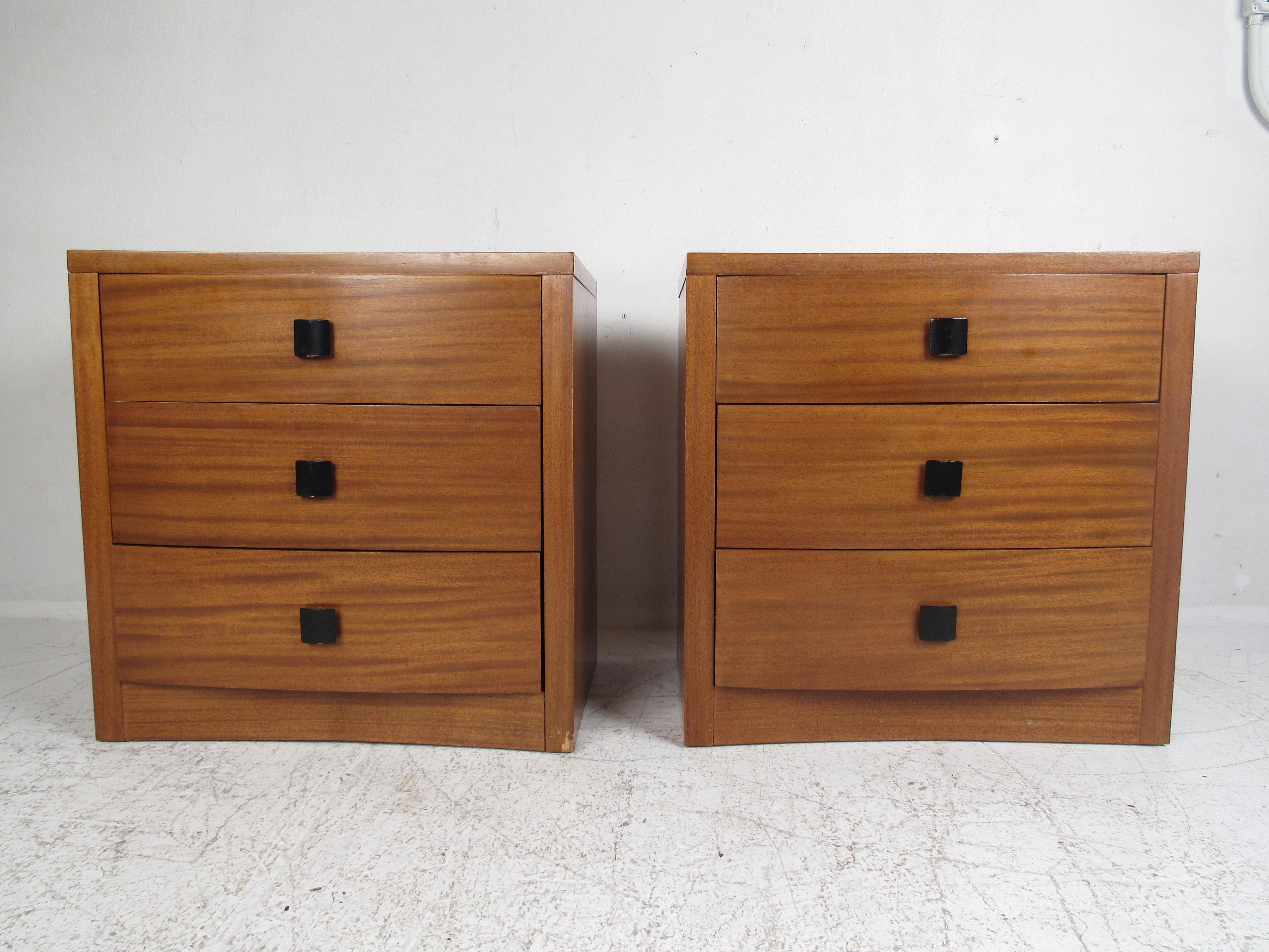 A beautiful pair of vintage modern chests with three drawers and beautiful walnut wood grain. This versatile pair of case pieces can function as nightstands or small dressers. A unique black painted square drawer pull and a curved front shows