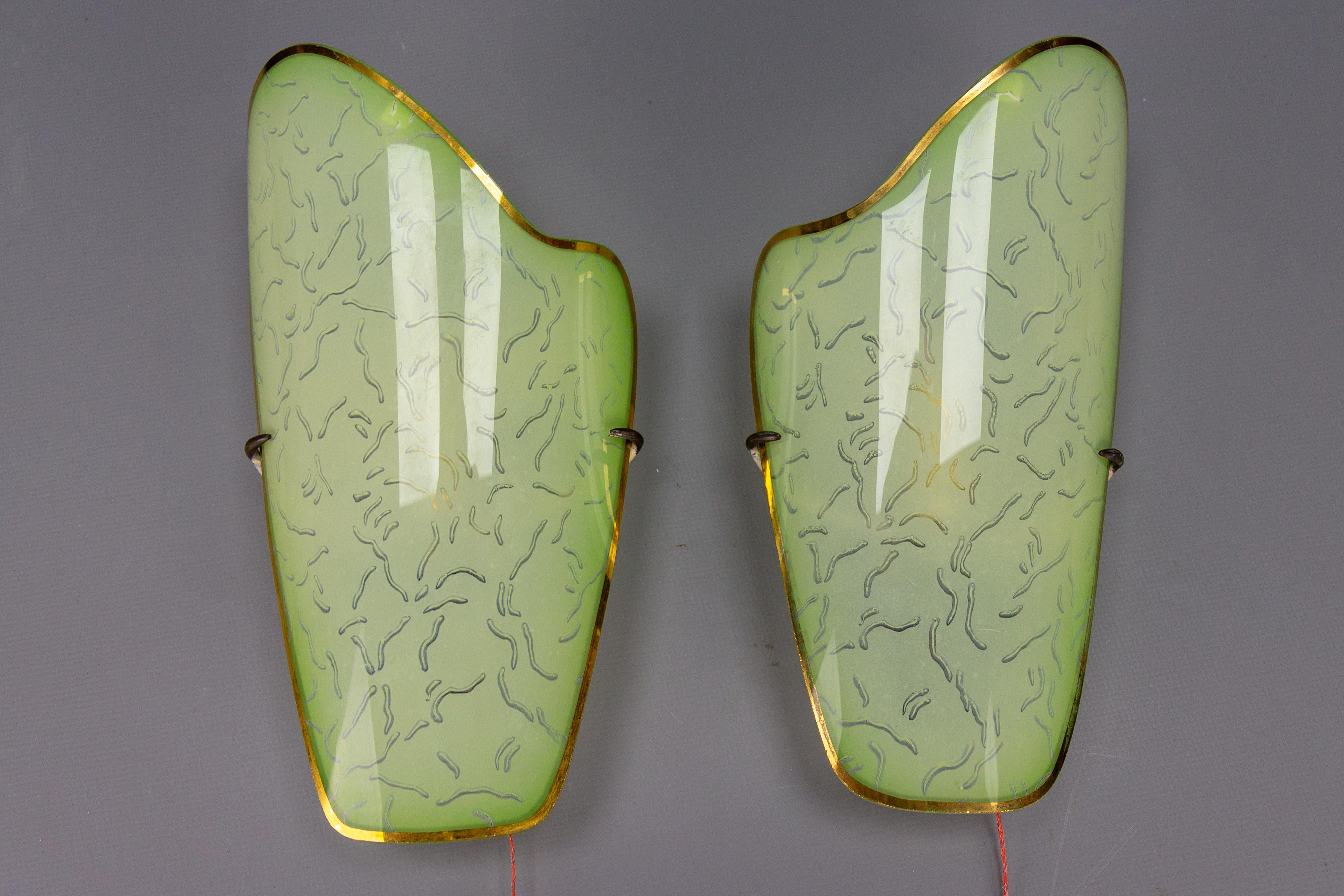 Pair of Mid-Century Modern curved green glass sconces, Germany, circa the 1950s.
This beautiful pair of sconces features curved green glass lampshades with a golden color edge. Each sconce has one new socket for an E14-size light bulb and a pull