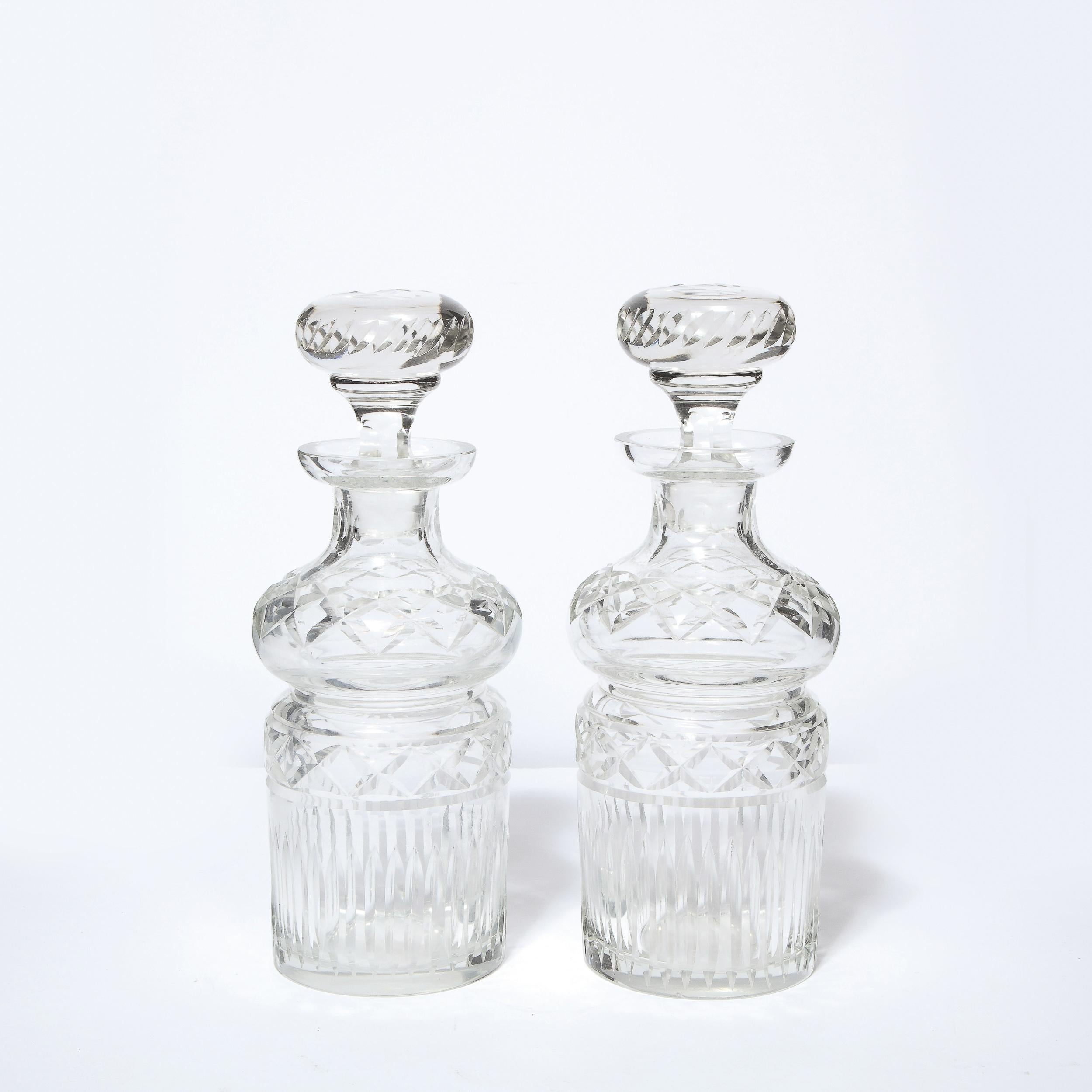 This stunning pair of Mid-Century Modern decanters were realized in the United States circa 1960. They features undulating cylindrical bodies- full of dynamic curves- with a wealth of geometric patterns etched into the body of each piece, including