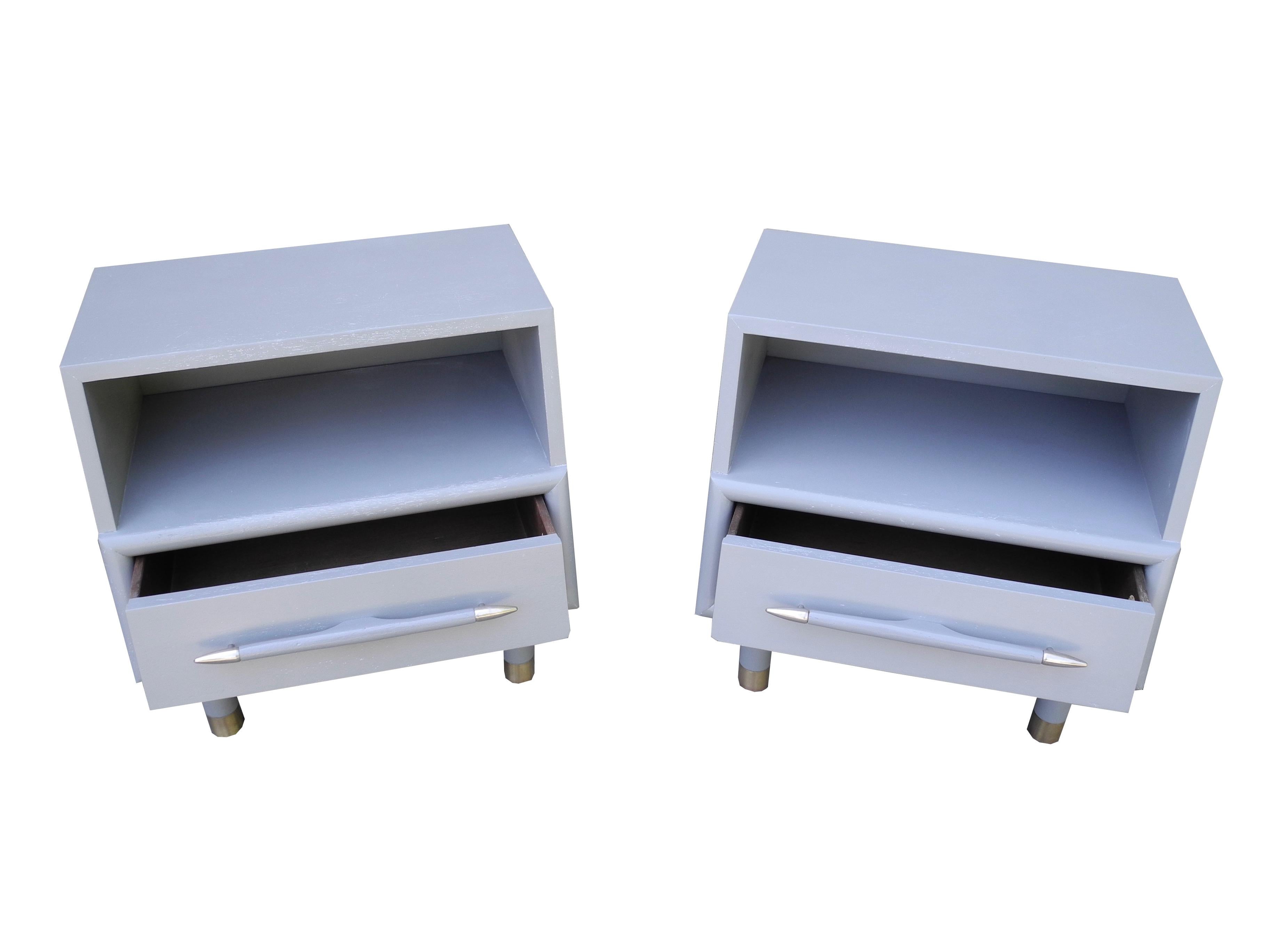 These Brown Saltman of California, 1950s designer nightstands are painted middle gray. They have brass sabots and silver metal hardware on the drawer handle. Equipped with a cubby and drawer, the profile slants from 11.5