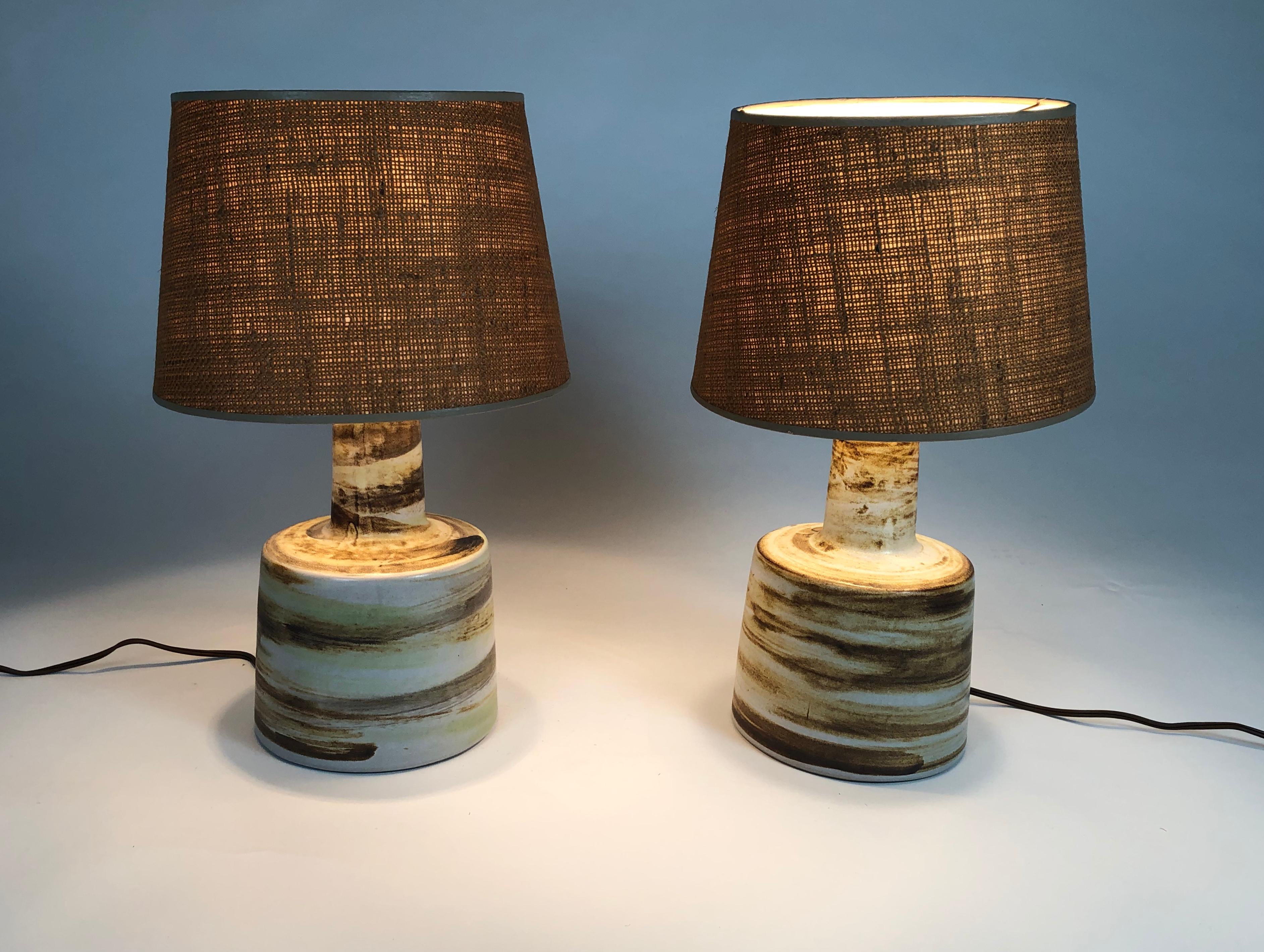 A pair of Jane and Gordon Martz art pottery lamps, each of stepped cylindrical form with a larger flared circular base and narrower neck on top, in white glazed ceramic, hand decorated with loosely applied brushwork in shades of brown, grey, tan