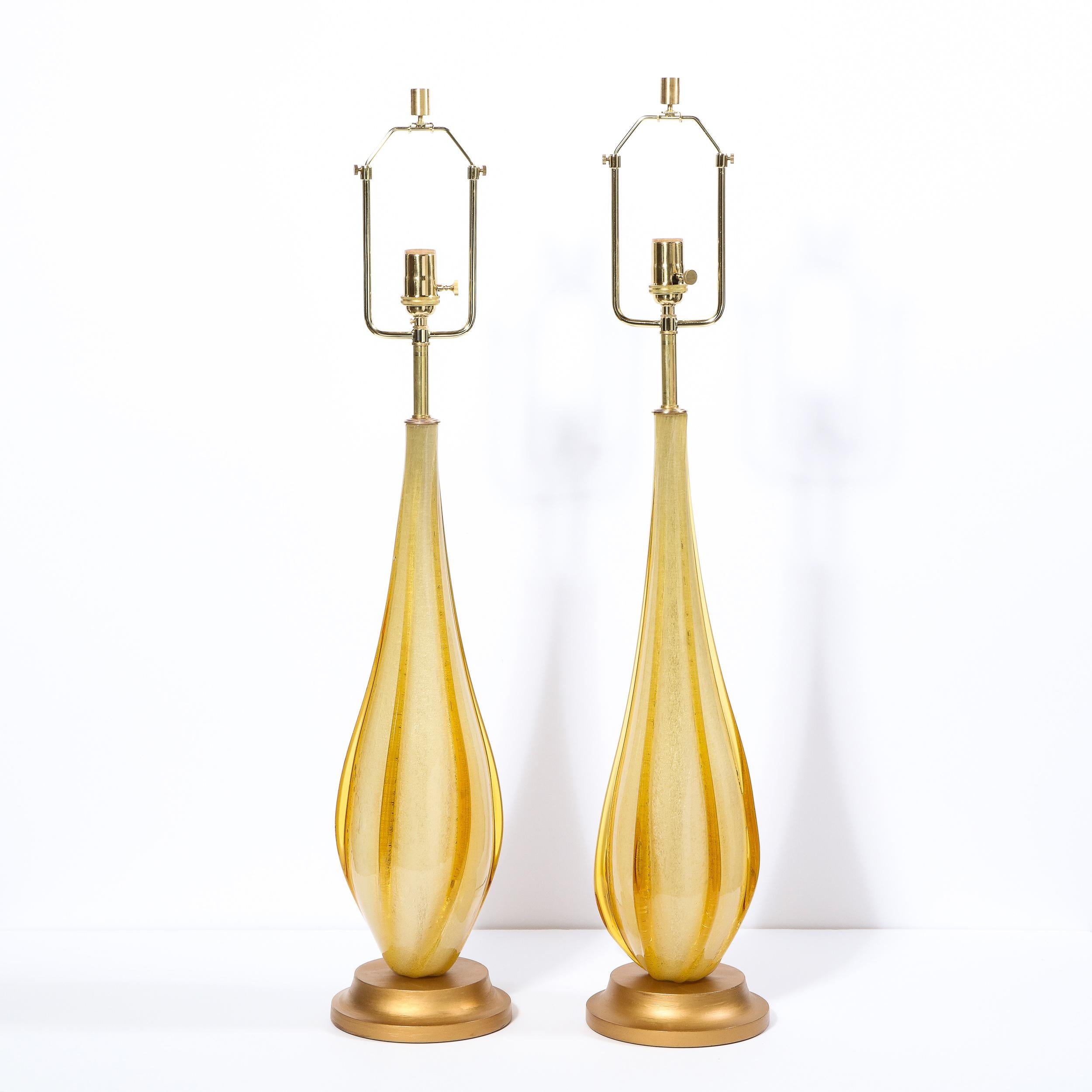 This stunning pair of Mid-Century Modern table lamps were realized in Murano, Italy- the island off the coast of Venice renowned for centuries for its superlative glass production- circa 1960. They features honey hued tear drop bodies with raised
