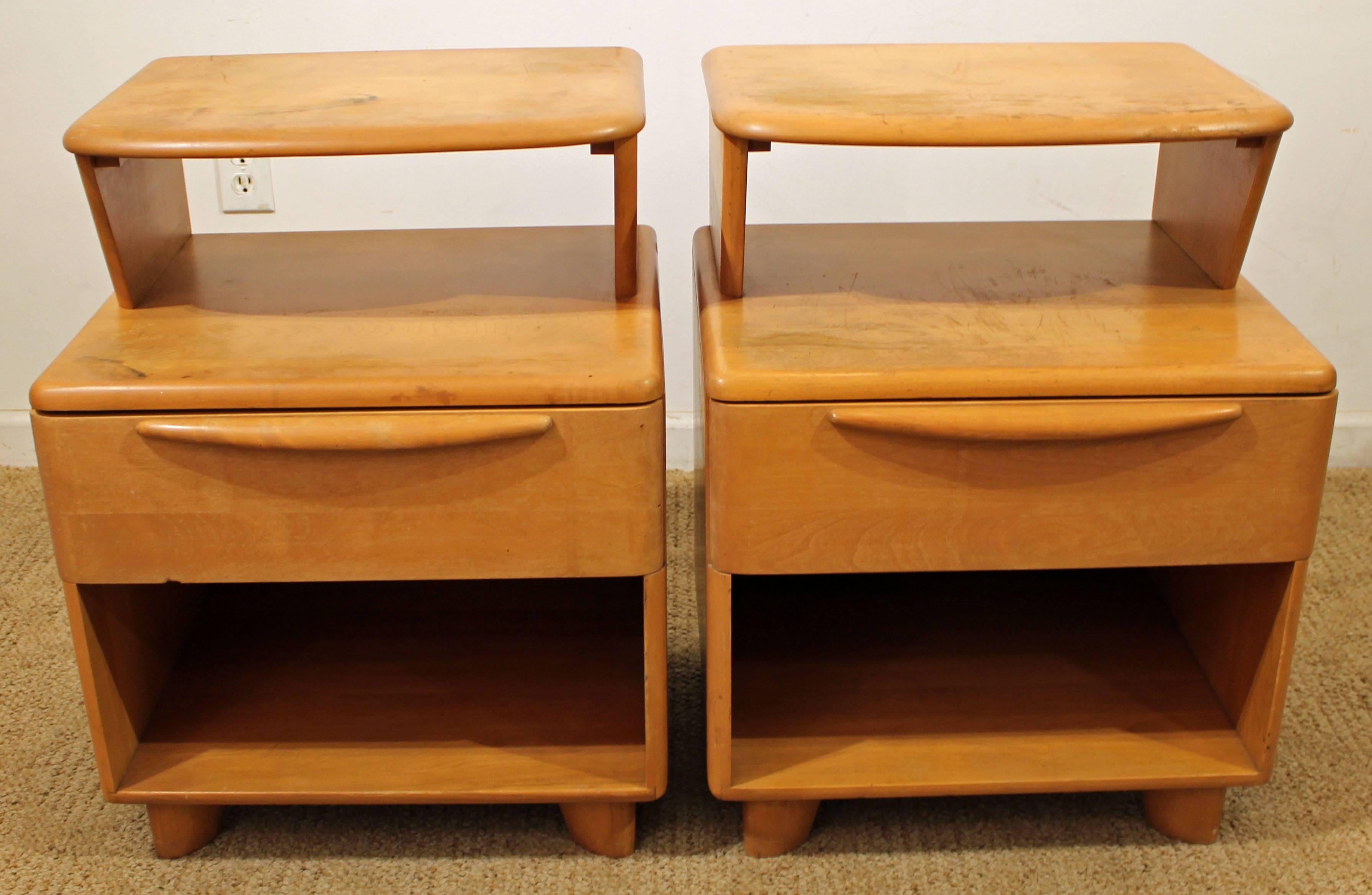 Offered is a pair of nightstands by Heywood-Wakefield. Each nightstand features one drawer and a shelf. The color is 'champagne'. They are in decent condition, but will need to be refinished. They are marked by Heywood-Wakefield.