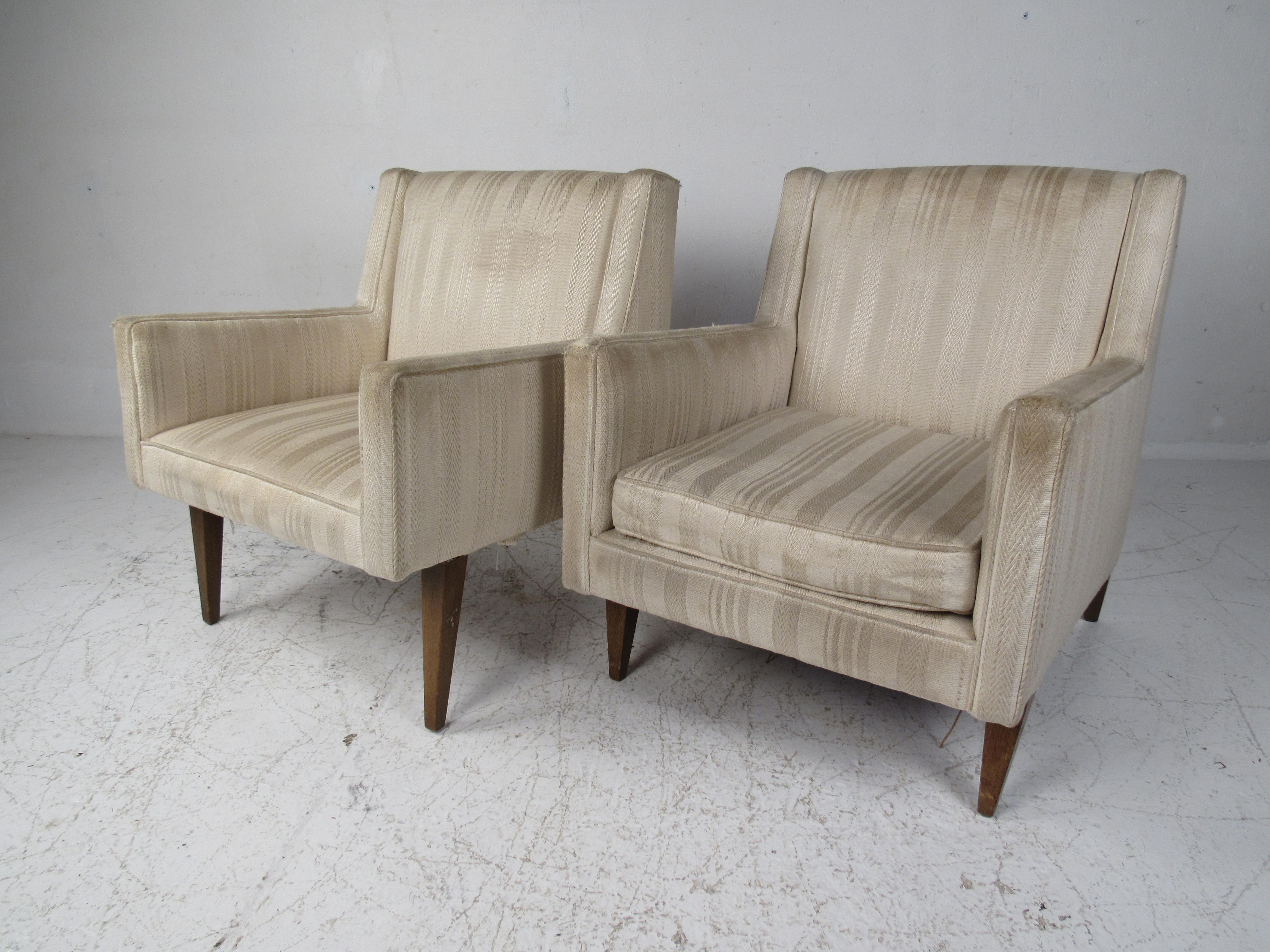 This beautiful pair of vintage modern armchairs boast different sized walnut legs and wide seating. A matching pair that has the same seat height even though one cushion is removable. A sleek and comfortable pair that is sure to make a lasting