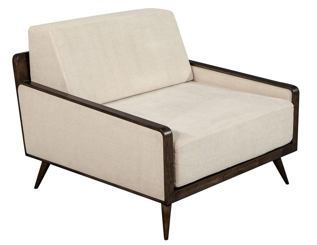 Pair of Mid-Century Modern inspired lounge chairs. Featuring oversized comfort design with sleek walnut colored frame. Finished in a beige textured fabric.
