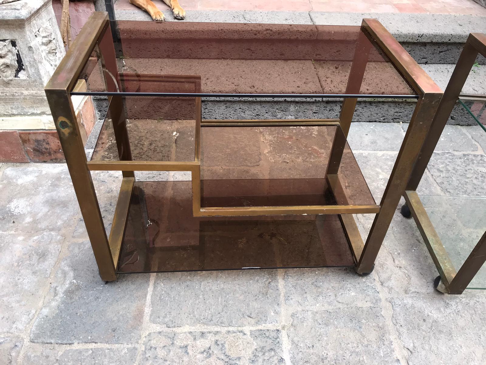 Pair of Mid-Century Modern etched bronze and glass bar or drinks cart. One cat is with clear glass shelves whereas  the other one is with smoked glass shelves.
These pieces are very elegant and would fit easily with any type of décor.
They can be