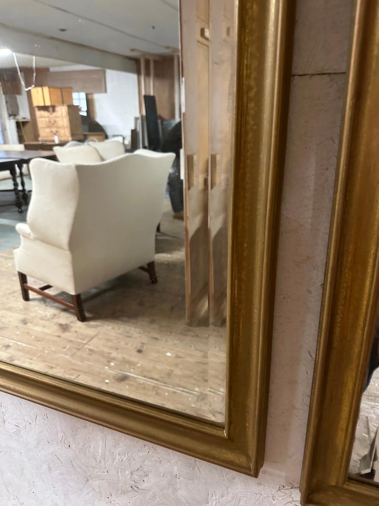 Pair of Mid-Century Modern Maison Jansen style mirror with gold gilt paint in a simple frame topped with a camel back, the mirrors will bring an undeniable touch of elegance to any wall -- hang in entry foyer, above console tables, credenza, or in a
