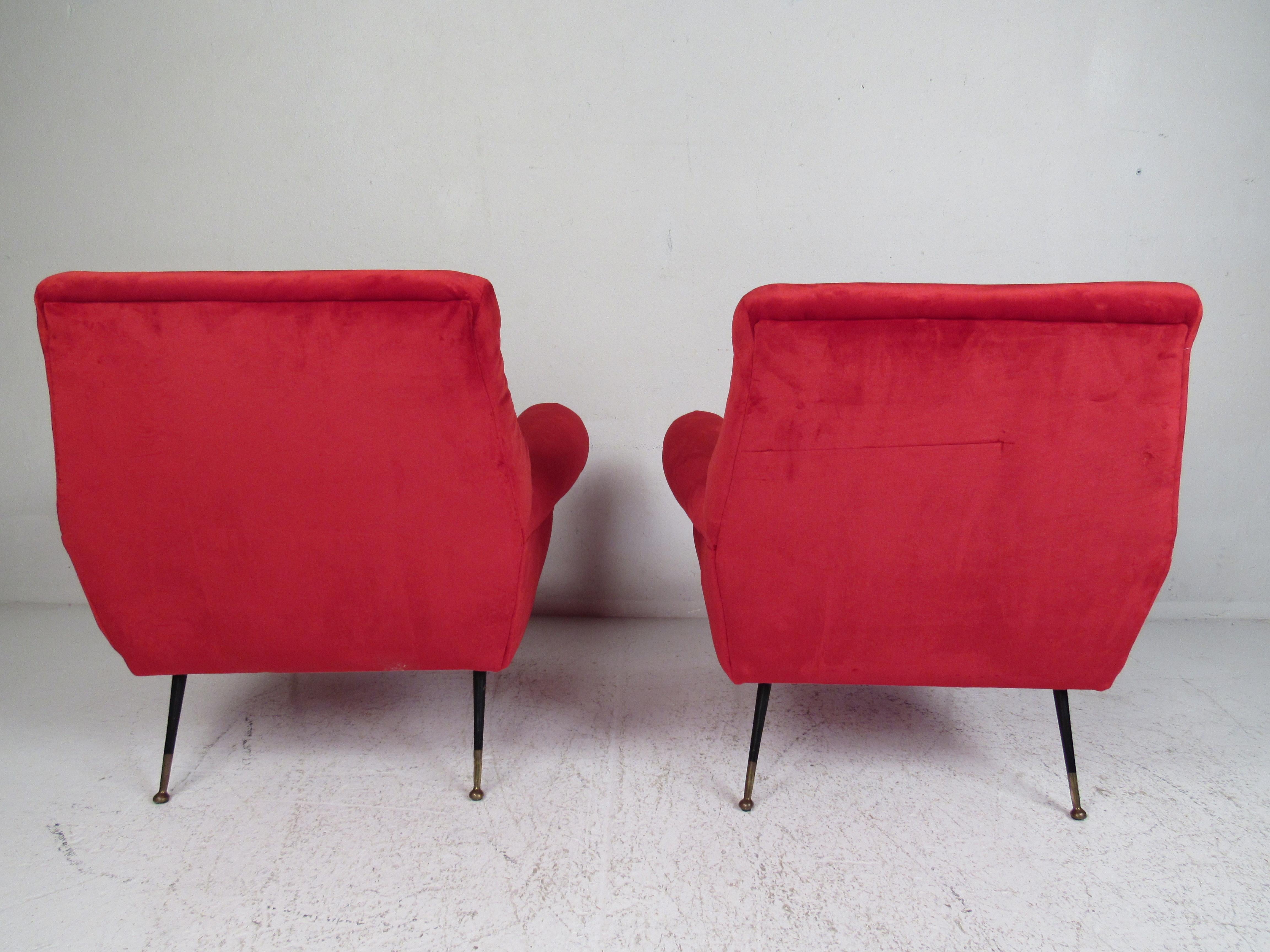 This beautiful pair of vintage modern lounge chairs feature thick padded seating covered in elegant ruby red upholstery. A sleek and comfortable low sitting design that has splayed metal legs with brass feet. The overstuffed armrests and wide