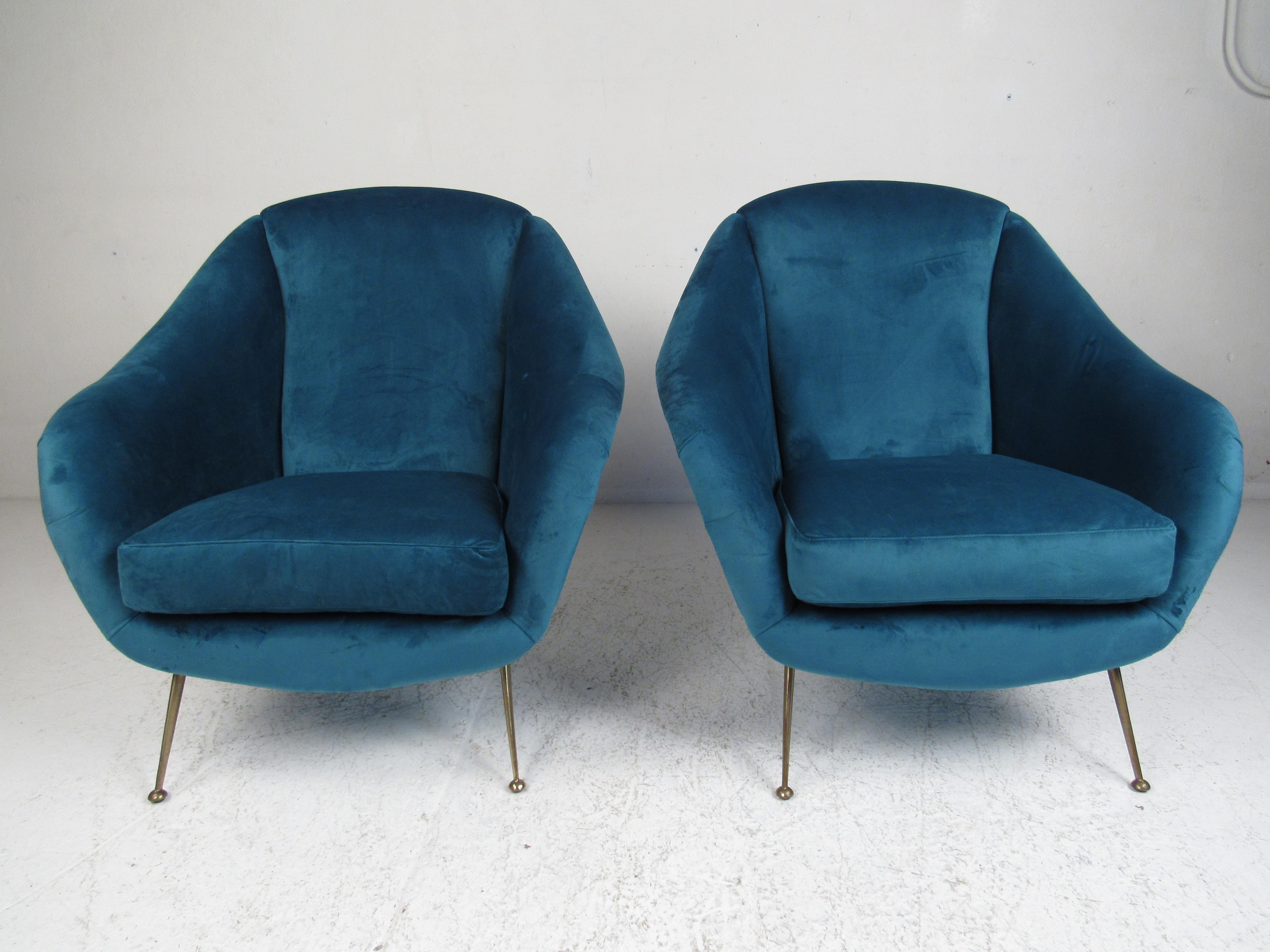 This elegant pair of vintage modern lounge chairs feature beautiful blue velour fabric and splayed brass legs. A sleek design in the style of Gio Ponti, that offers maximum comfort in any seating arrangement. The sloped armrests, drumstick shaped