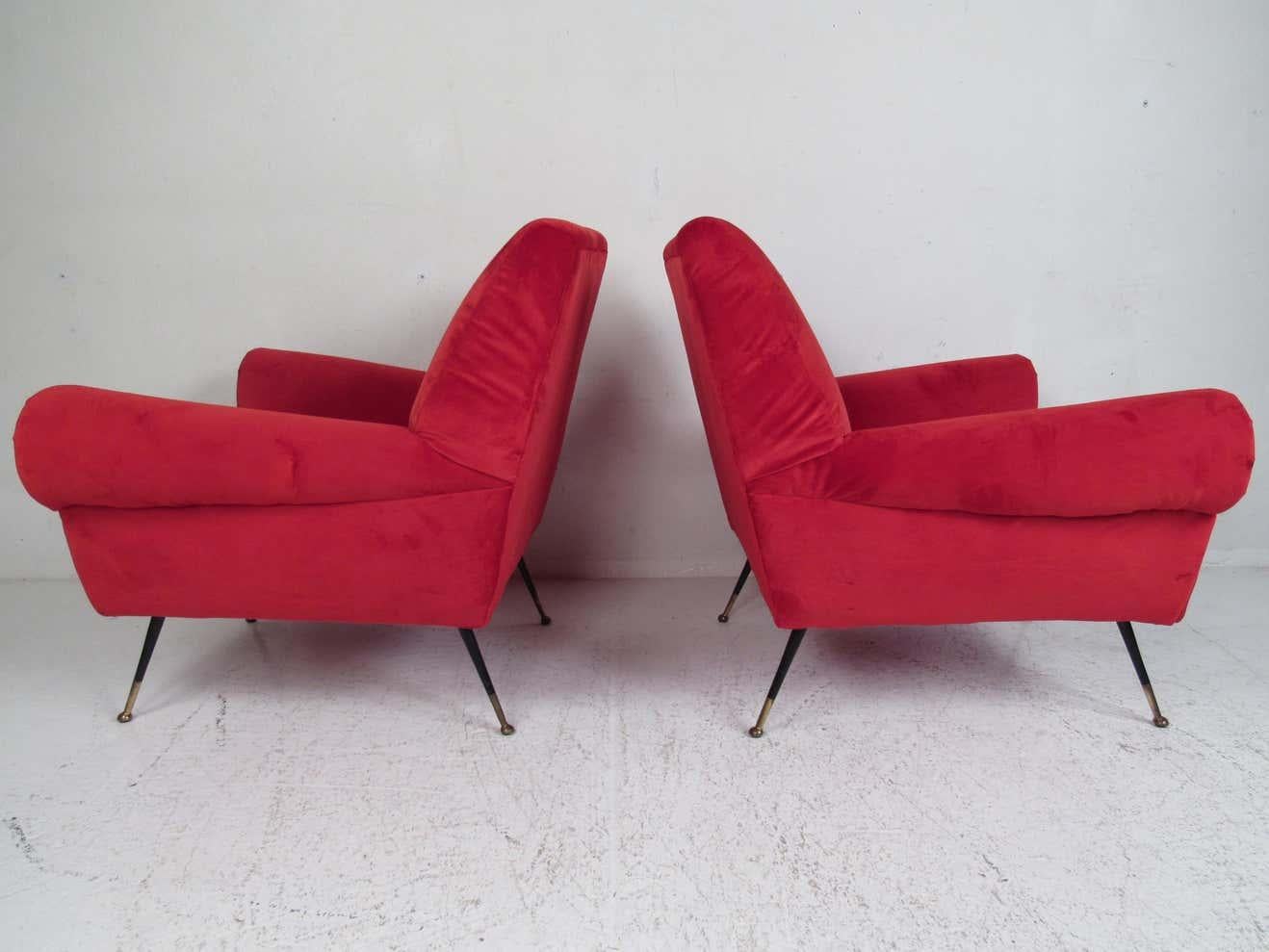 This beautiful pair of vintage modern lounge chairs feature thick padded seating covered in elegant ruby red upholstery. A sleek and comfortable low sitting design that has splayed metal legs with brass feet. The overstuffed armrests and wide