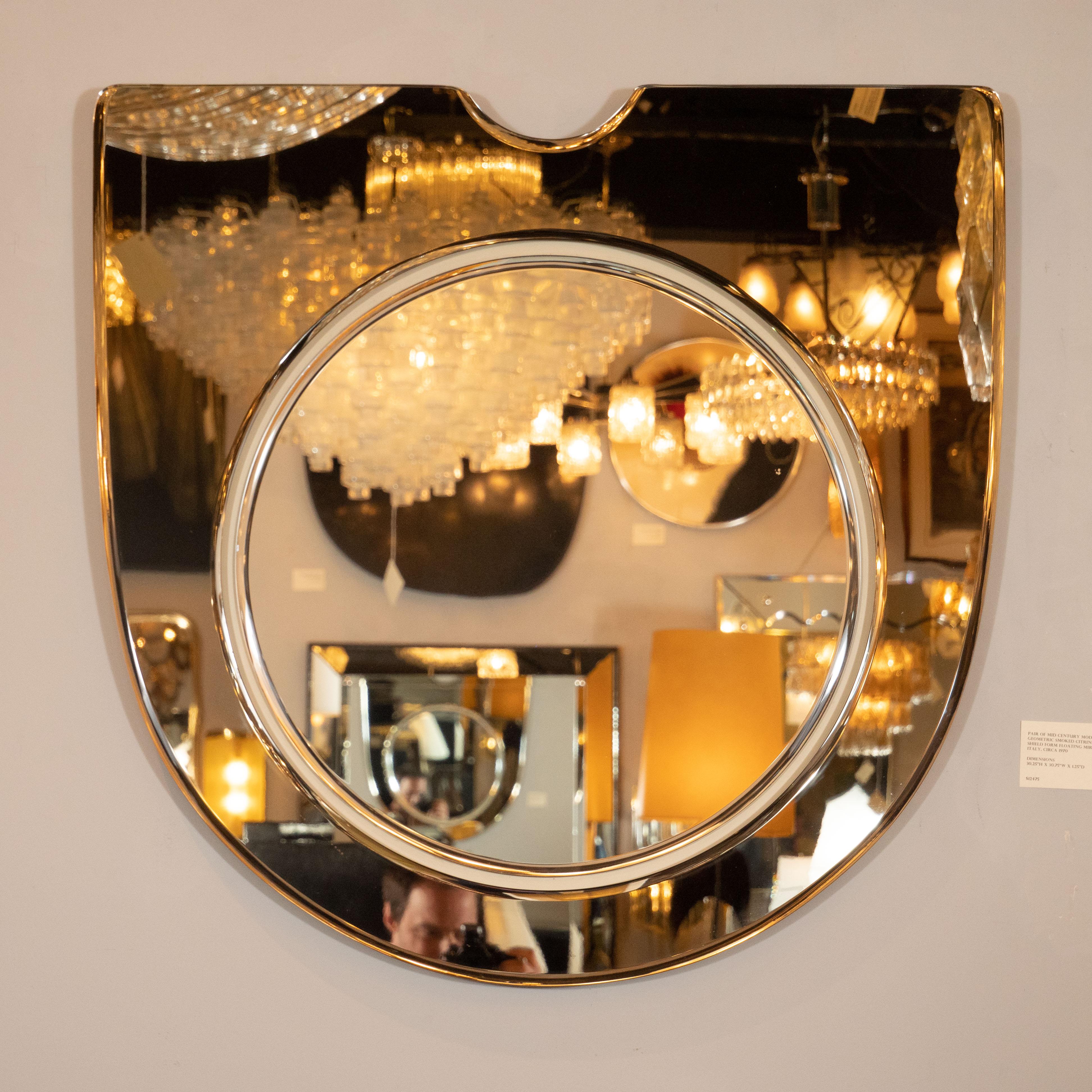 This stunning and graphic pair of Mid-Century Modern mirrors were realized in Italy, circa 1970. They feature a shield form consisting of a bowed body with a flat top notched in the center with a demilune form. Floating in the center of this form-