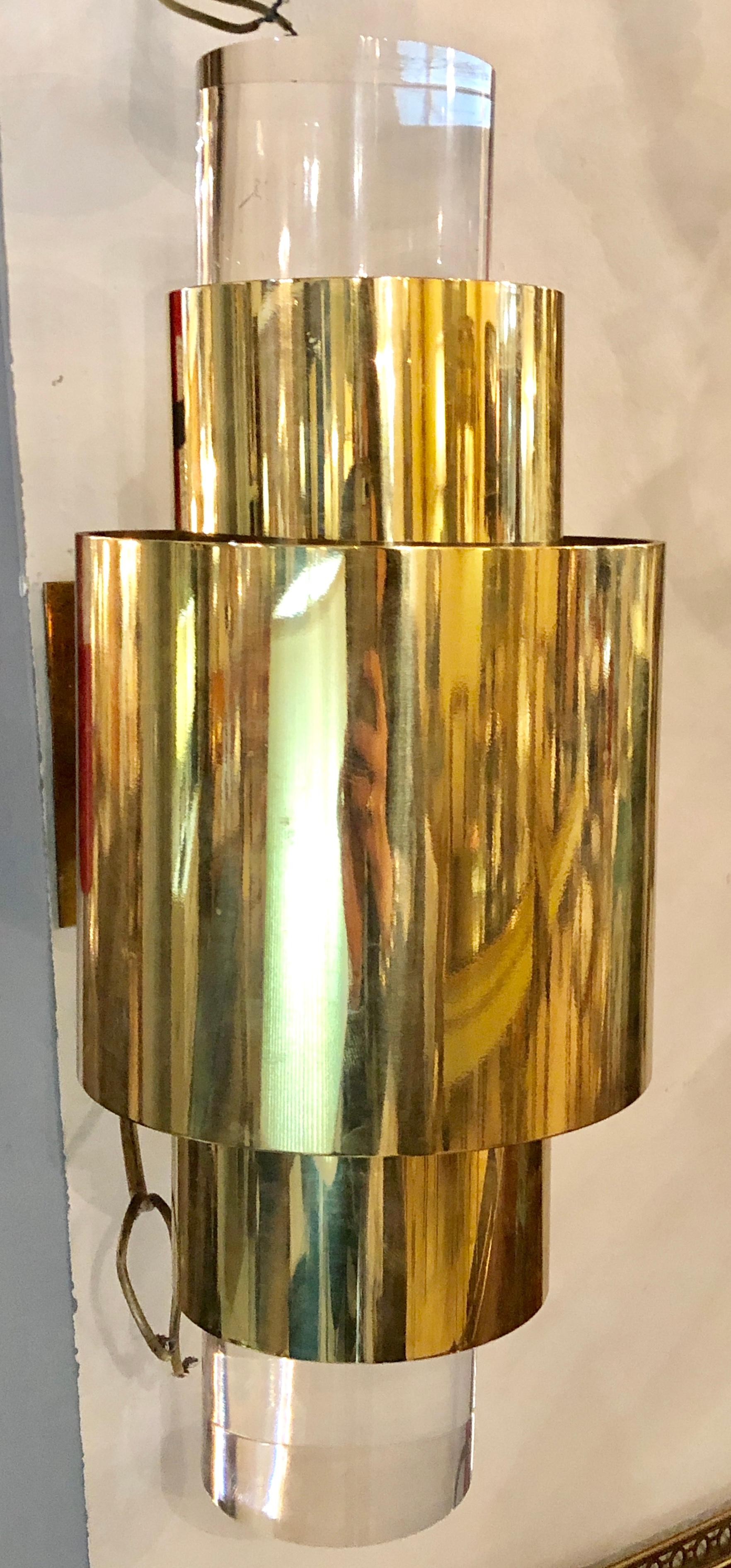Pair of brass and Lucite wall sconces. These sleek and stylish Mid-Century Modern wall sconce of wall lights have large think Lucite tubular decorated tops and bottoms sitting inside the brass tubular frames. The pair having strong brass wall plates.