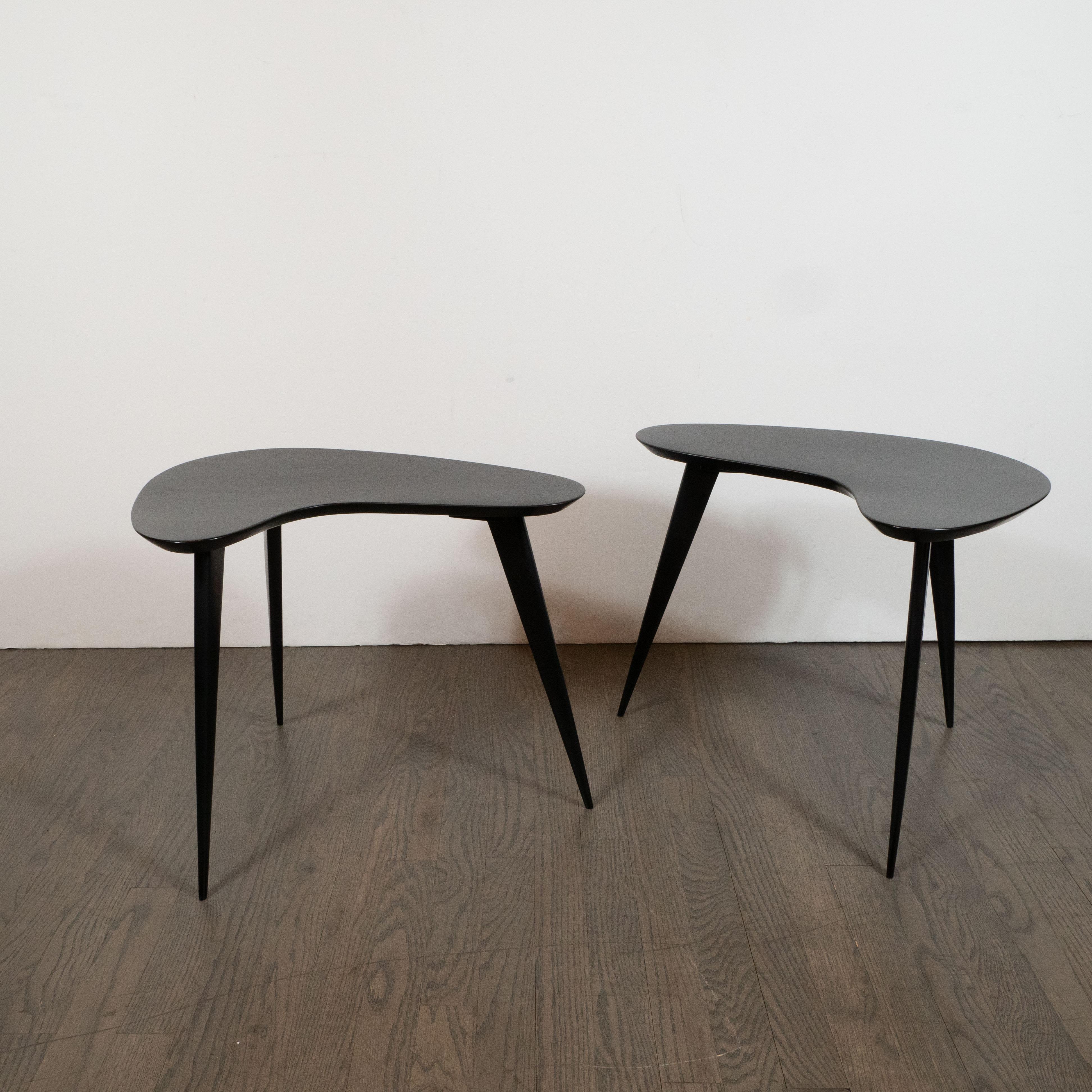 This stunning and graphic pair of Mid-Century Modern side tables were realized in the United States, circa 1950. They feature amorphic kidney shaped tops and conical legs all realized in ebonized walnut. With their neutral palate and clean modernist