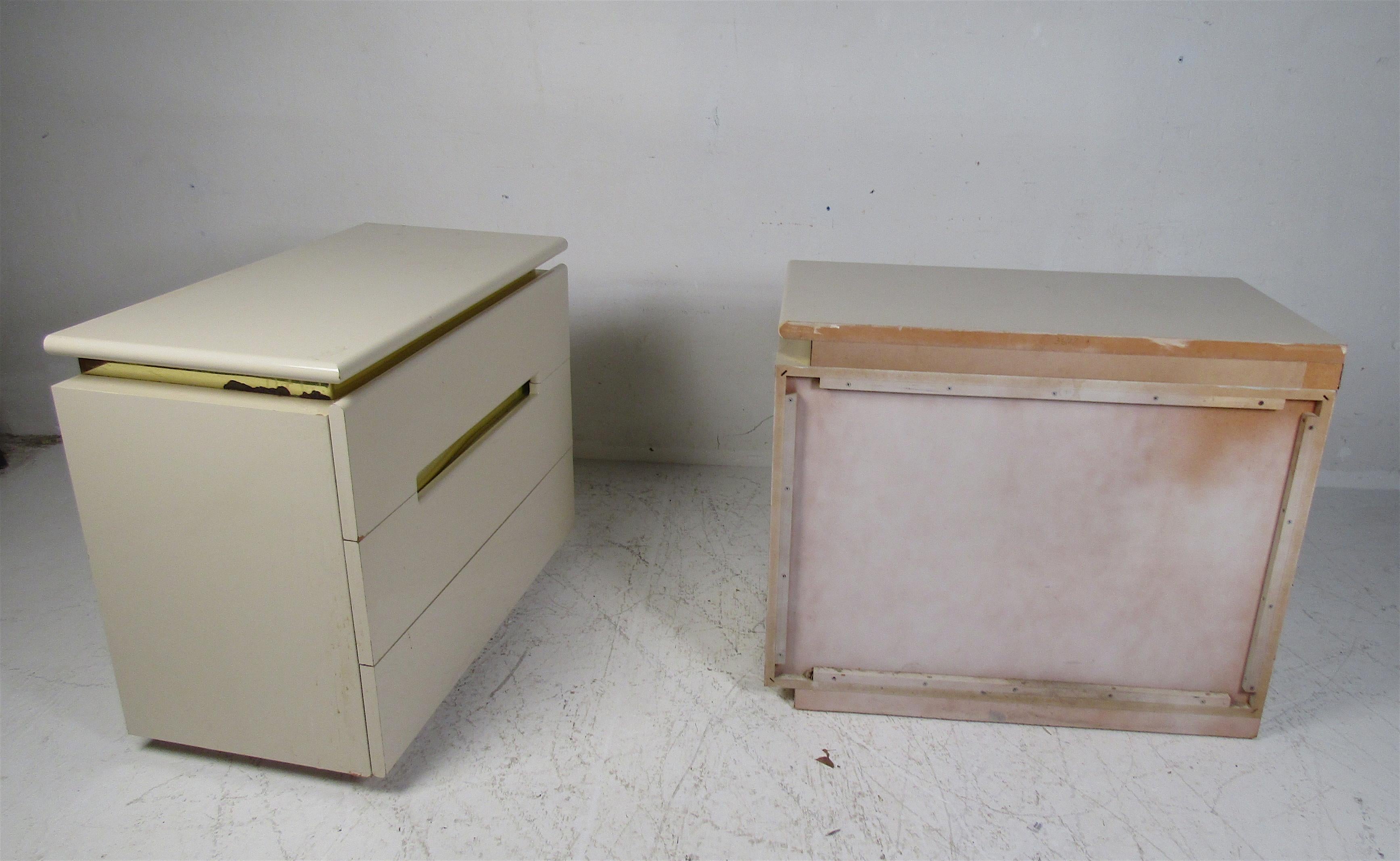 A beautiful pair of vintage modern chests with brass trim and raised tops. This stylish pair offers ample storage space within its three hefty drawers. The beautiful off-white color with a lacquered finish adds to the midcentury appeal. Please
