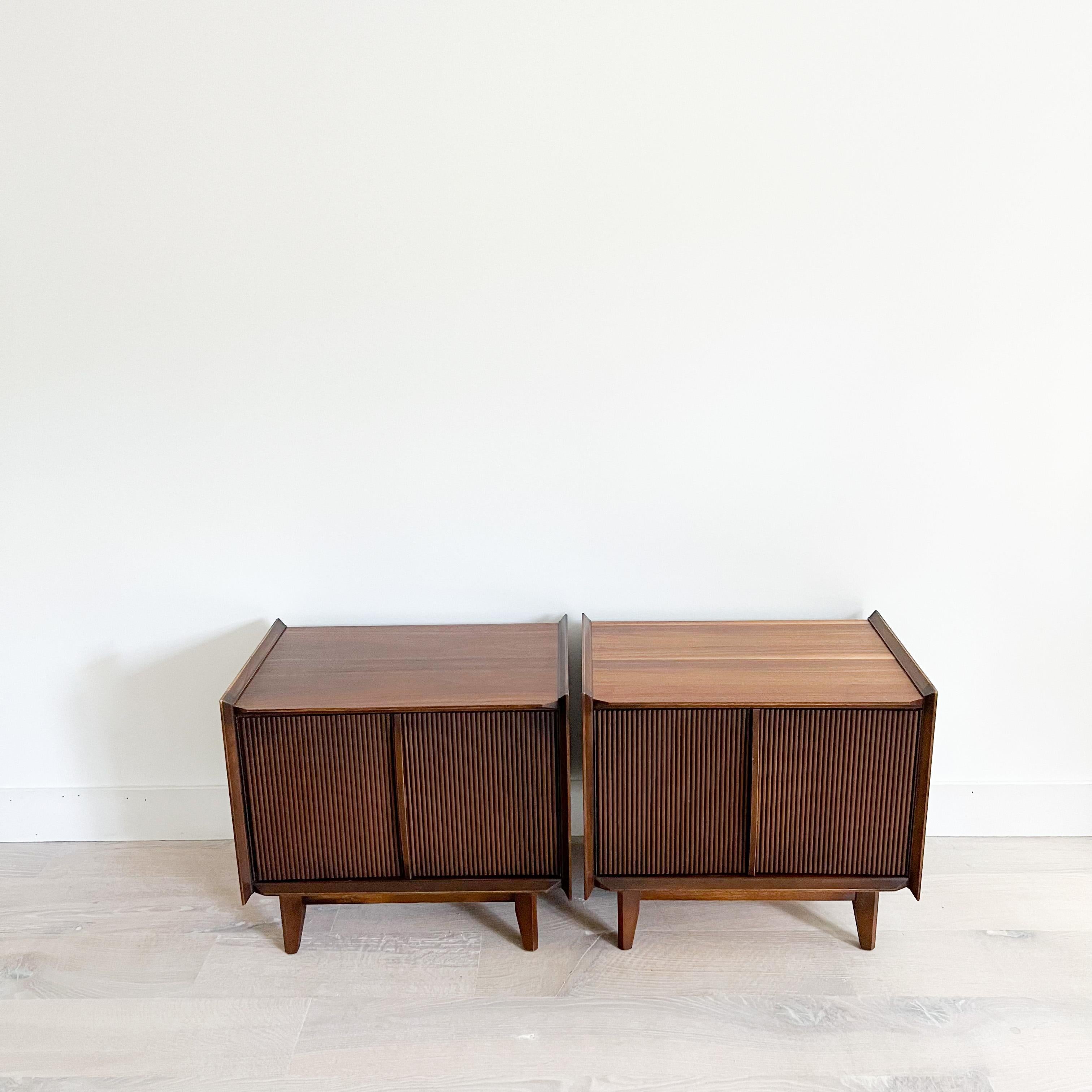 Pair of Mid-Century Modern walnut nightstands by Lane 1st Edition. The tops have been sanded and restored. Some light scuffing/scratching and small areas of veneer repair from age appropriate wear. The cabinet doors open and close with ease.
