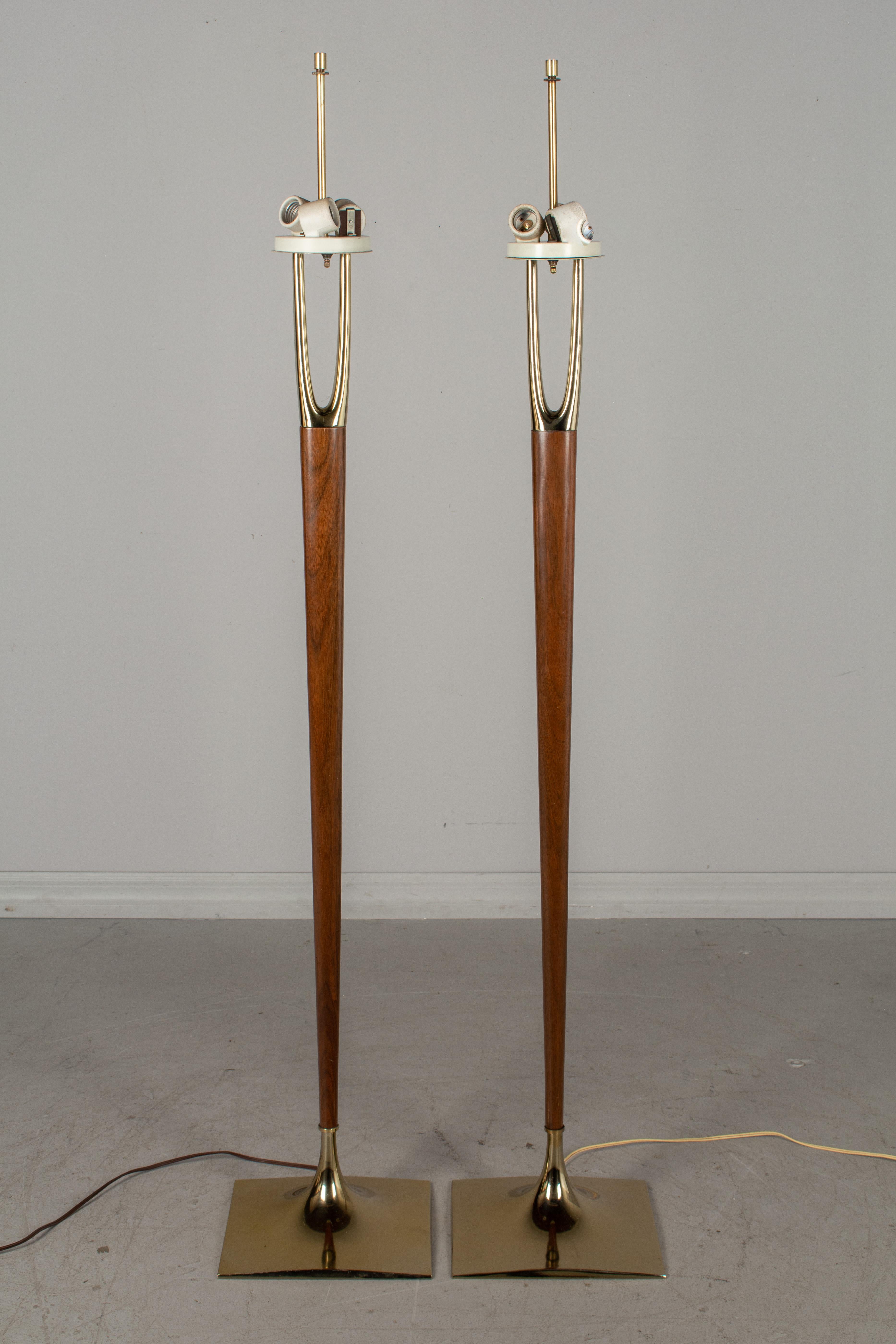A rare pair of iconic, sought after Mid-Century Modern floor lamps designed by Gerald Thurston and made by the Laurel Lamp Company. Solid walnut center post with brass-plated wishbone shaped prong at top and a brass-plated base. Original three-way