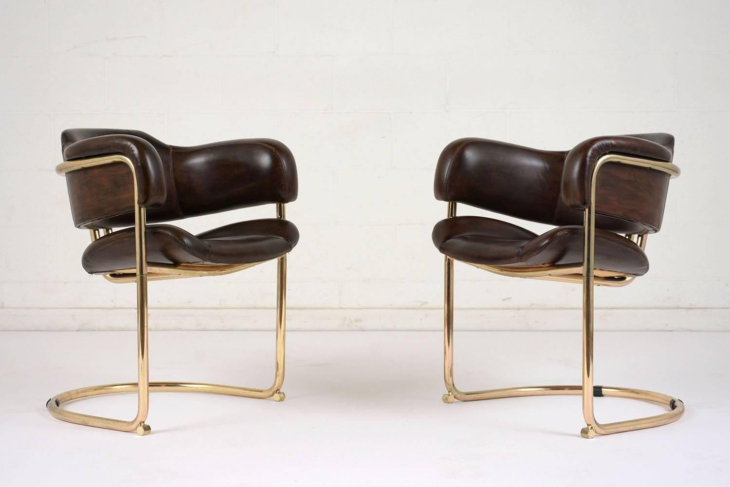 This pair of 1960s Mid-Century Modern-style armchairs features brass frames and comfortable leather seats. The brass frames have a floating seat with a curved back and supports. The seats are upholstered in leather dyed a deep brown color with