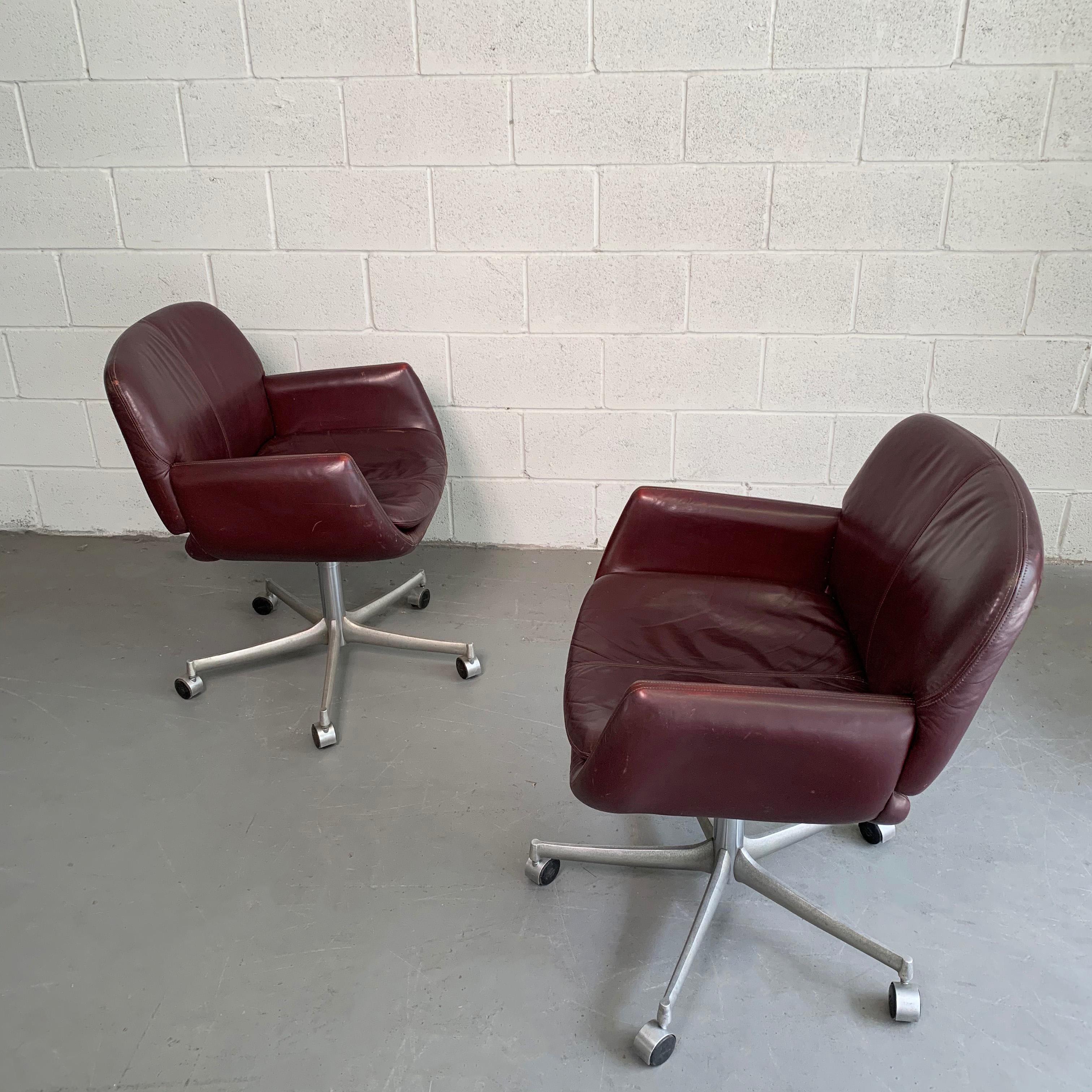 Pair of Mid-Century Modern, office armchairs feature burgundy leather, swivel seats on rolling aluminum bases.