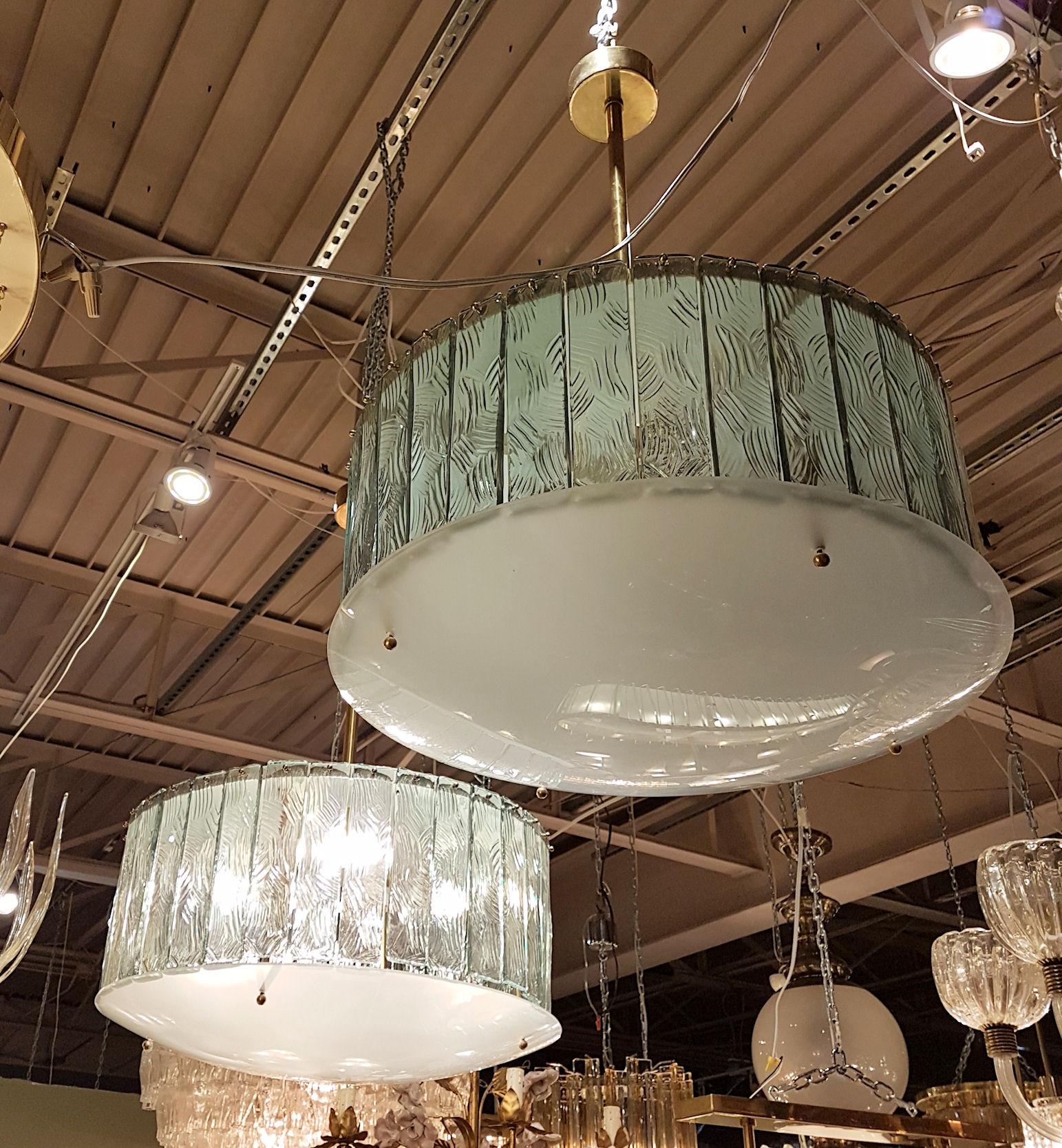 Pair of Mid-Century Modern light green/translucent glass and brass chandeliers, in the style of Gio Ponti, by Fontana Arte, Italy. 
The vintage drum chandeliers have 4 candelabra base lights each and are rewired for the US.
The light green glasses