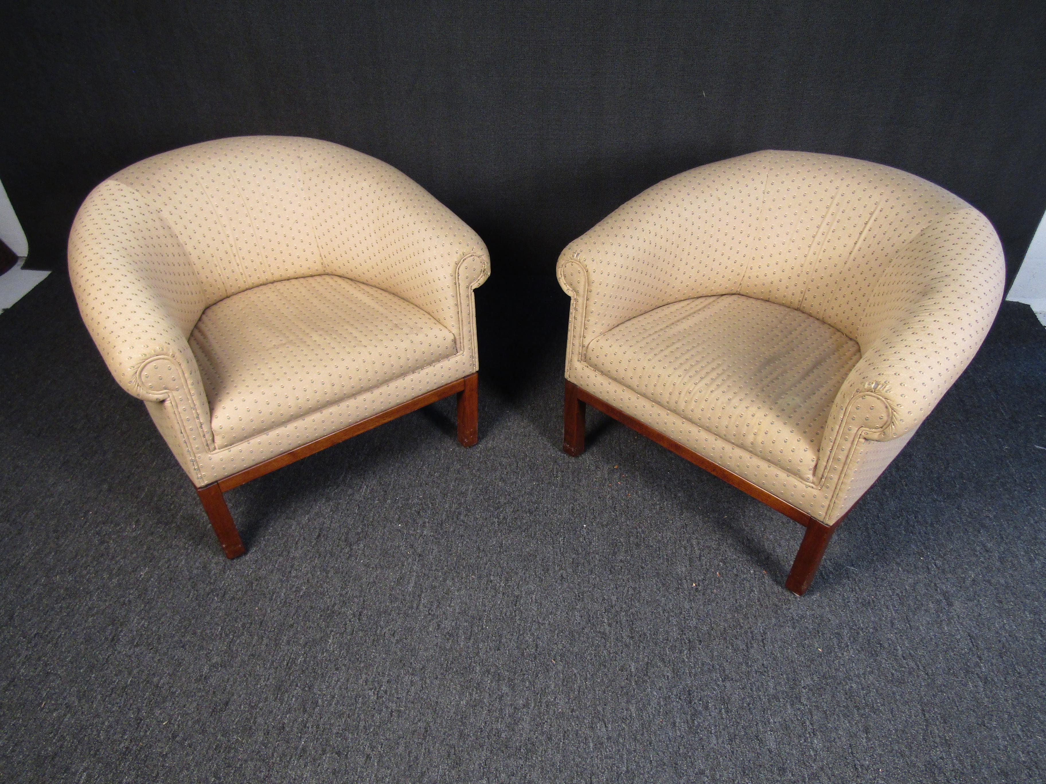 A pair of Mid-Century Modern lounge chairs that feature a subtle yet stylish upholstery complemented by a wooden frame and legs. The rounded and cushioned shape of the chairs offers comfort in classic Mid-Century style. Please confirm item location