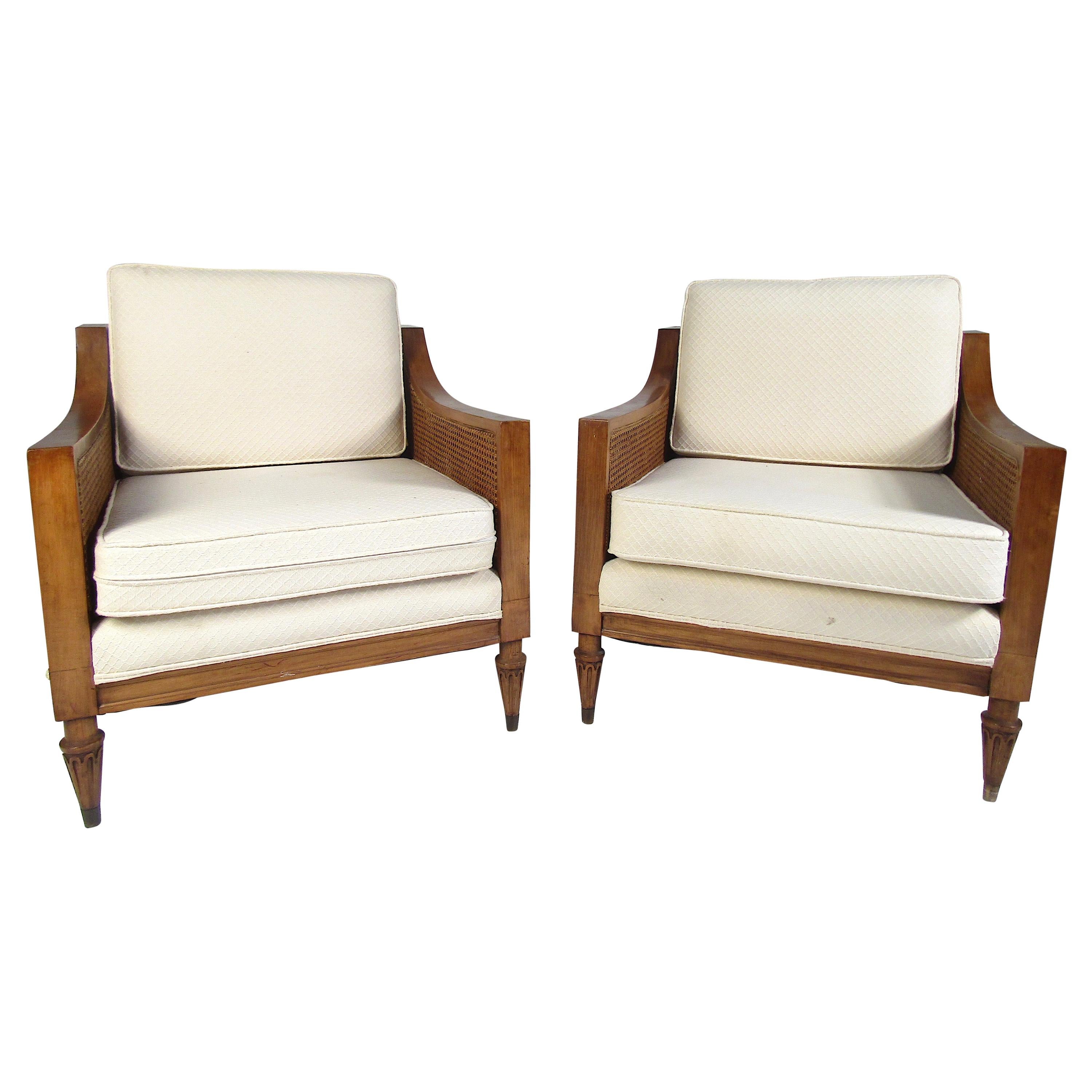 This beautiful pair of vintage lounge chairs feature cane sides and a sturdy walnut frame. The thick padded cushions with off-white upholstery and sloped armrests ensure maximum comfort. This sleek pair of armchairs make the perfect addition to any