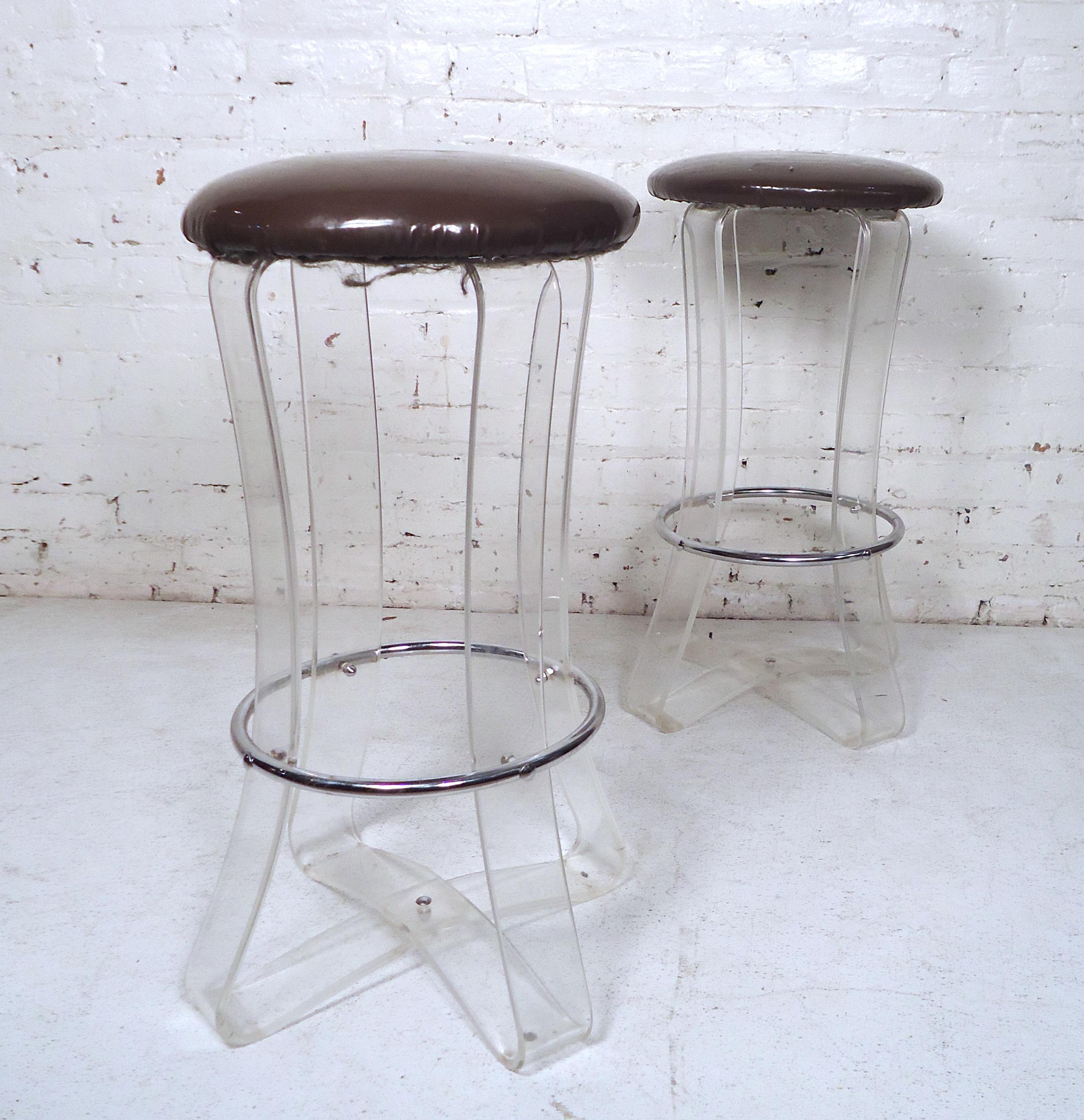 Unique pair of Mid-Century Modern Lucite stools featuring a metal footrest and vinyl seating.

(Please confirm item location NY or NJ with dealer).