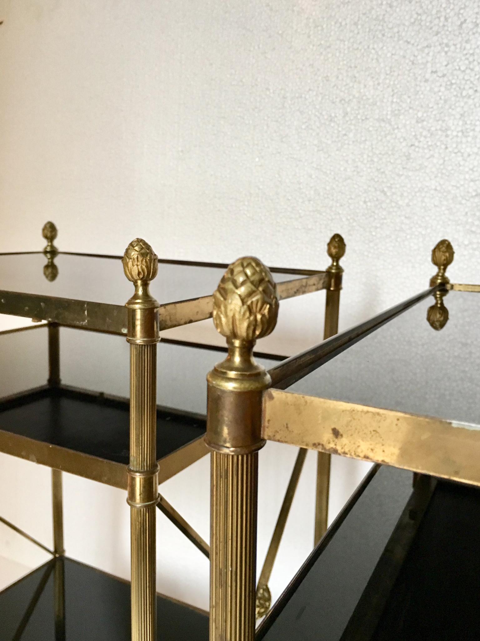 Pair of midcentury brass three-tier etageres Maison Jansen style, with brass finished, and black glass , and X-frame side.