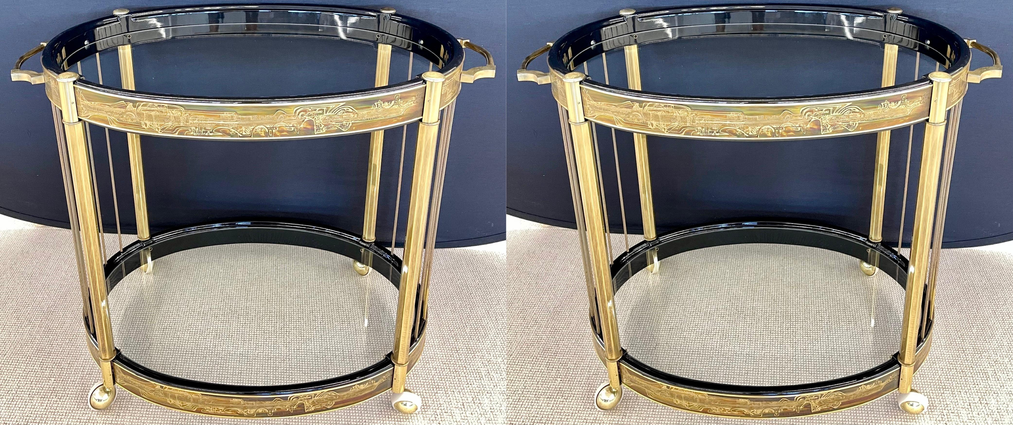 A pair of Mid-Century Modern master-craft brass acid etched bar-carts or serving wagons. This one of a kind pair of simply stunning bar carts or servers has two oval glass polished edge shelves supported by a pair of aprons all having wonderful acid
