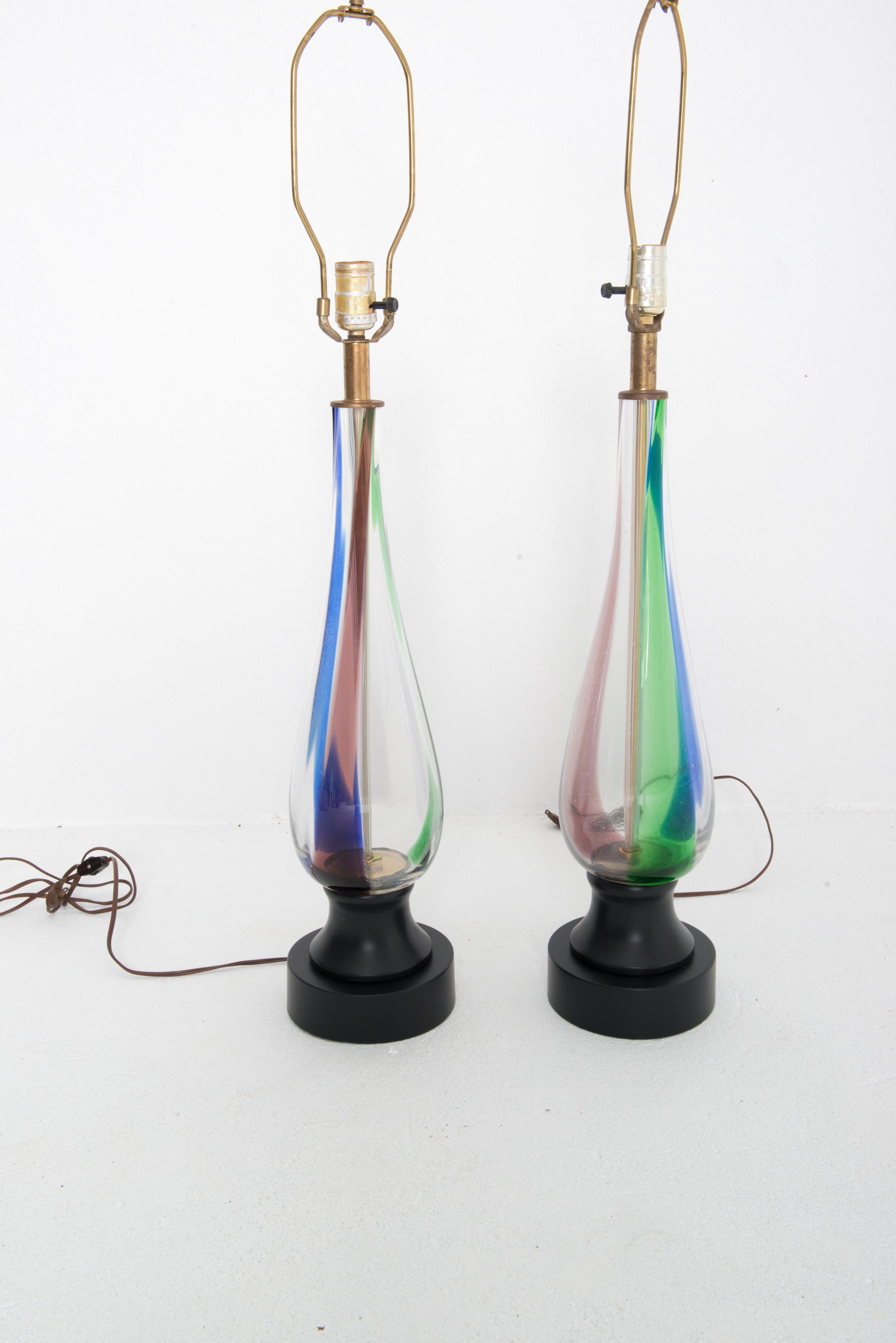 Pair of Mid-Century Modern blown glass table lamps with multi color vertical streaks within the glass. Harps and finials are included. Round black painted metal bases. No shades.