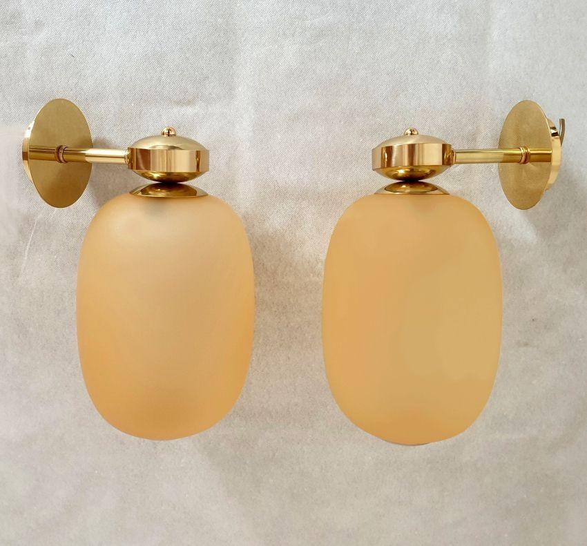 Pair of Mid-Century-Modern Murano glass and brass sconces, Barovier & Toso style, Italy, 1980s.
Two pairs of sconces available. Priced and sold by pair.
Each sconce has a Murano glass globe, oval shape, in amber color and translucent.
Creates a warm