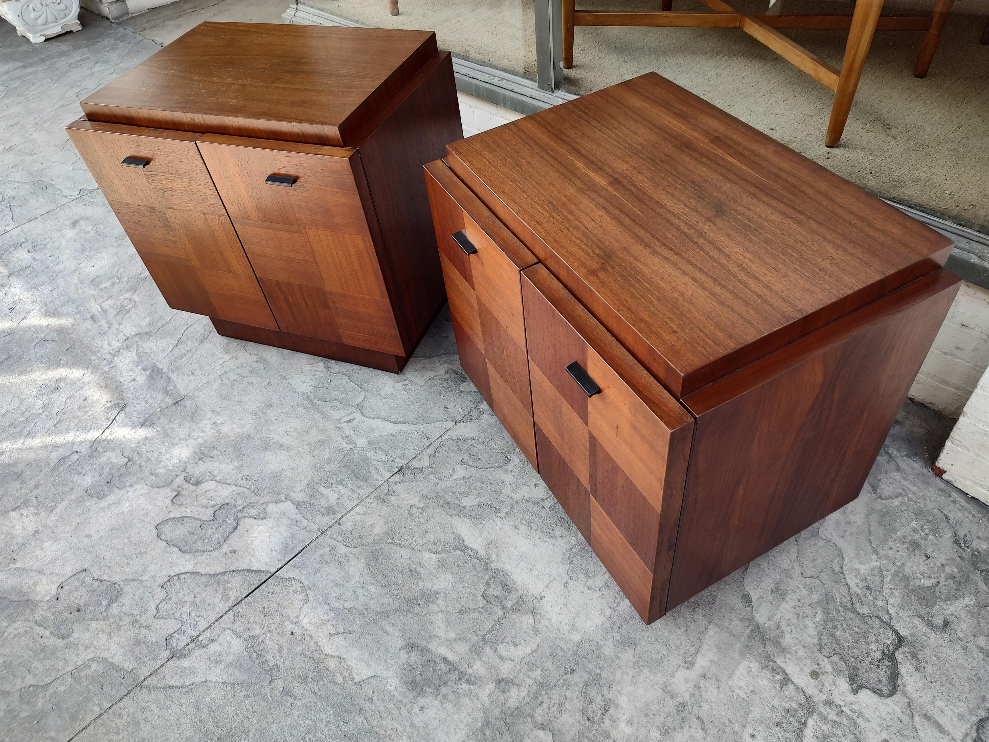 Fabulous pair of night tables by Lane, Staccato series. Brutalist styling, walnut squares cross stacked like a chess board across the double doors. Cabinet sits atop a plinth base. Black pulls contrasting. One Shelf inside for storage. Cabinets have