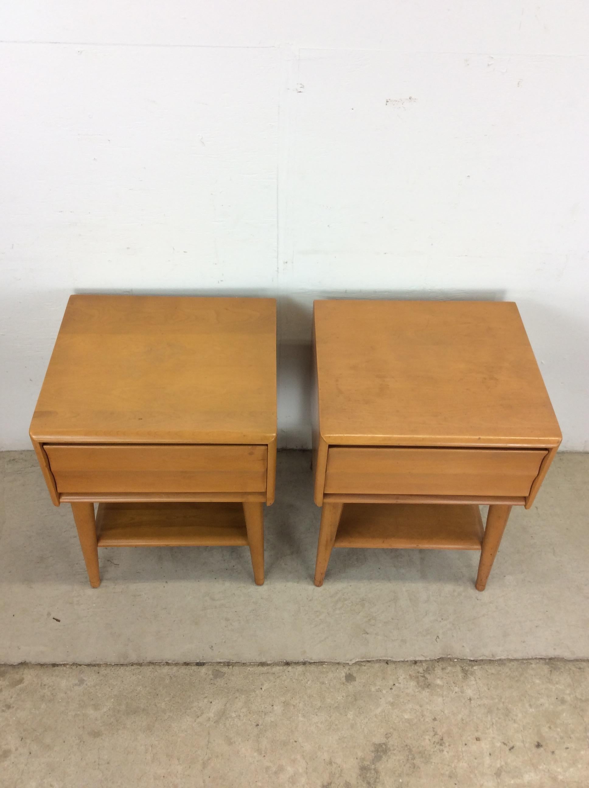 This pair of mid century modern nightstands by Heywood Wakefield features hardwood construction, original champagne finish, single dovetailed drawer with unique drawer face, opened shelf down below, and tall tapered legs.    Matching lowboy dresser