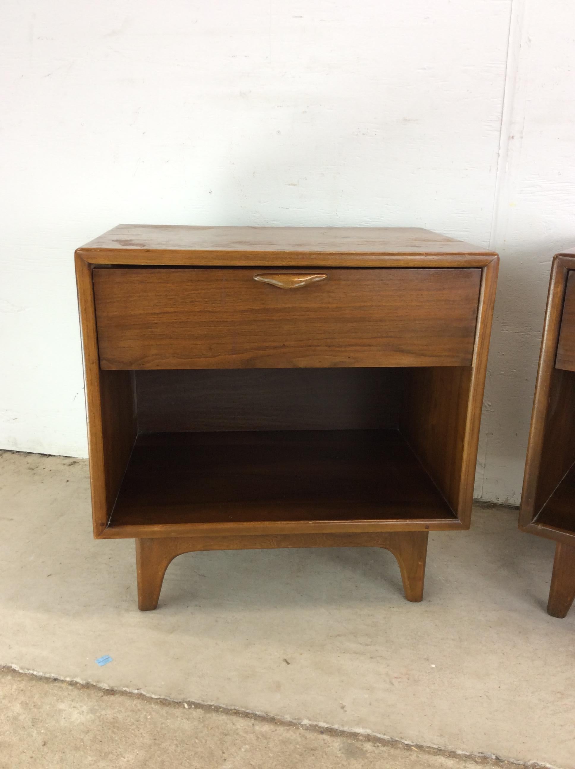 This pair of mid century modern nightstands from the Perspective line by Lane Furniture features hardwood construction, beautiful walnut veneer with original finish, single dovetailed drawer with unique curved wood pull, open storage shelf, and