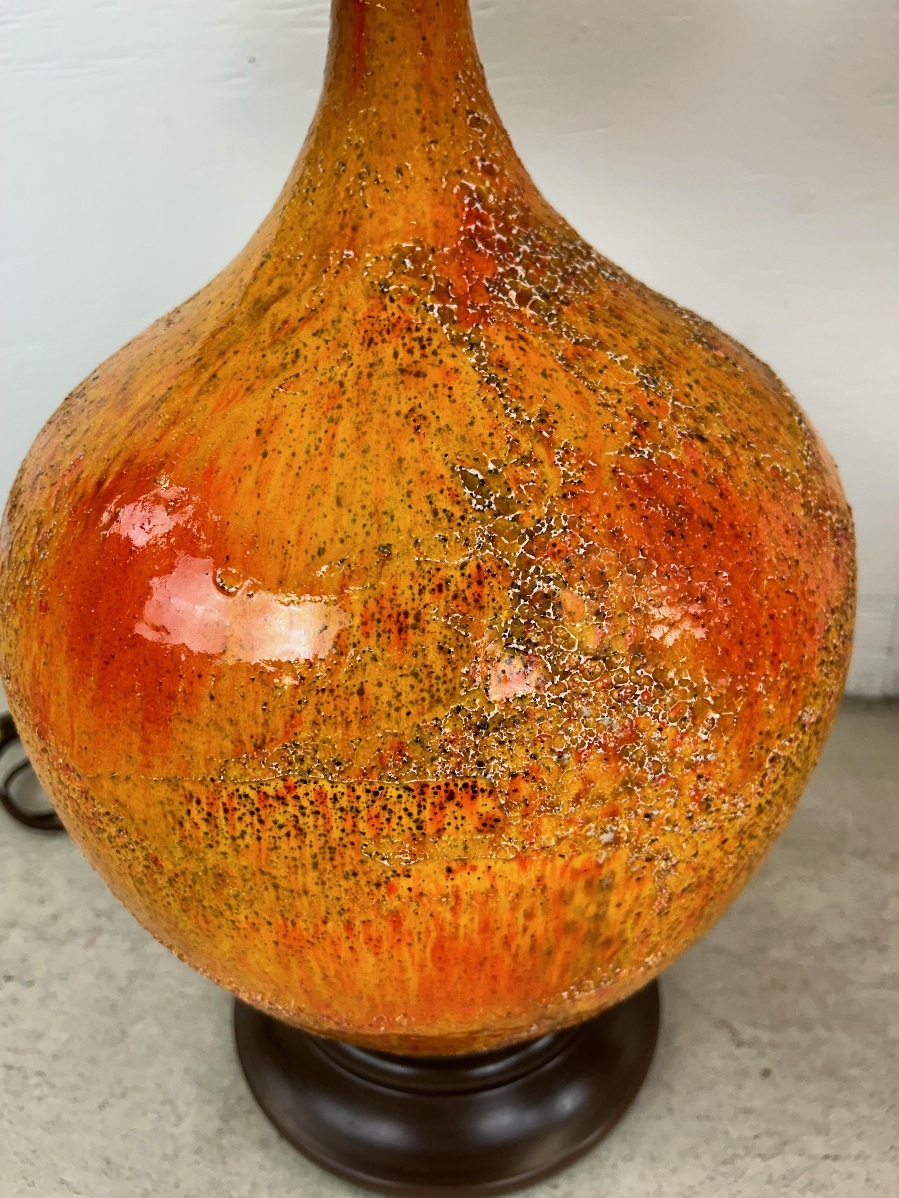 Cette paire de lampes de table modernes du milieu du siècle présente un corps en céramique de forme unique, une belle glaçure de lave avec orange, rouge et jaune, des abat-jours vintage plissés et un socle en bois arrondi. u2028u2028Les dimensions