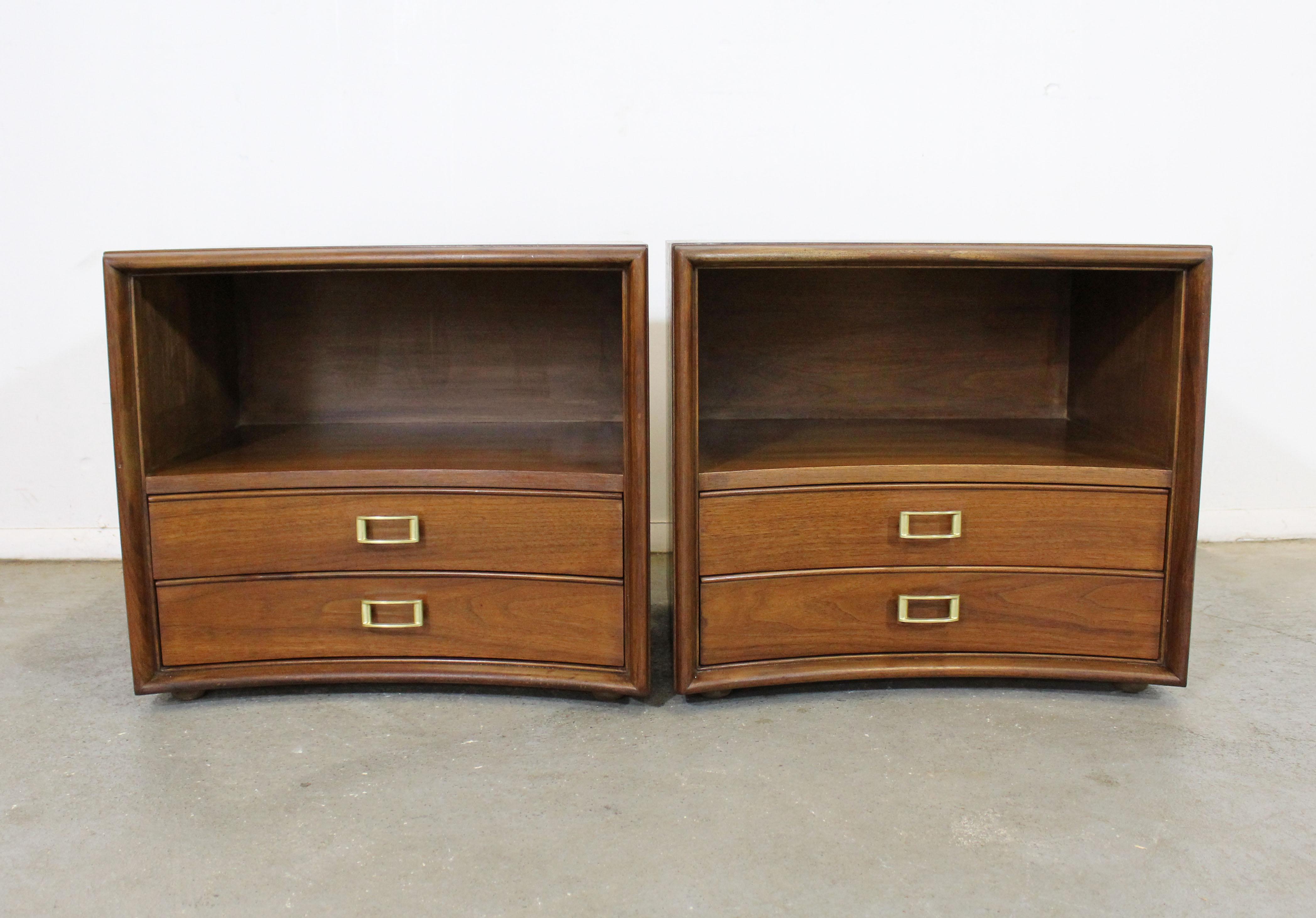 Offered is a pair of Mid-Century Modern nightstands designed by Paul Frankl for Johnson Furniture's 'Emissary' line. These stands feature curved fronts, two drawers each, and brass hardware. They have been refinished with a walnut stain. In very