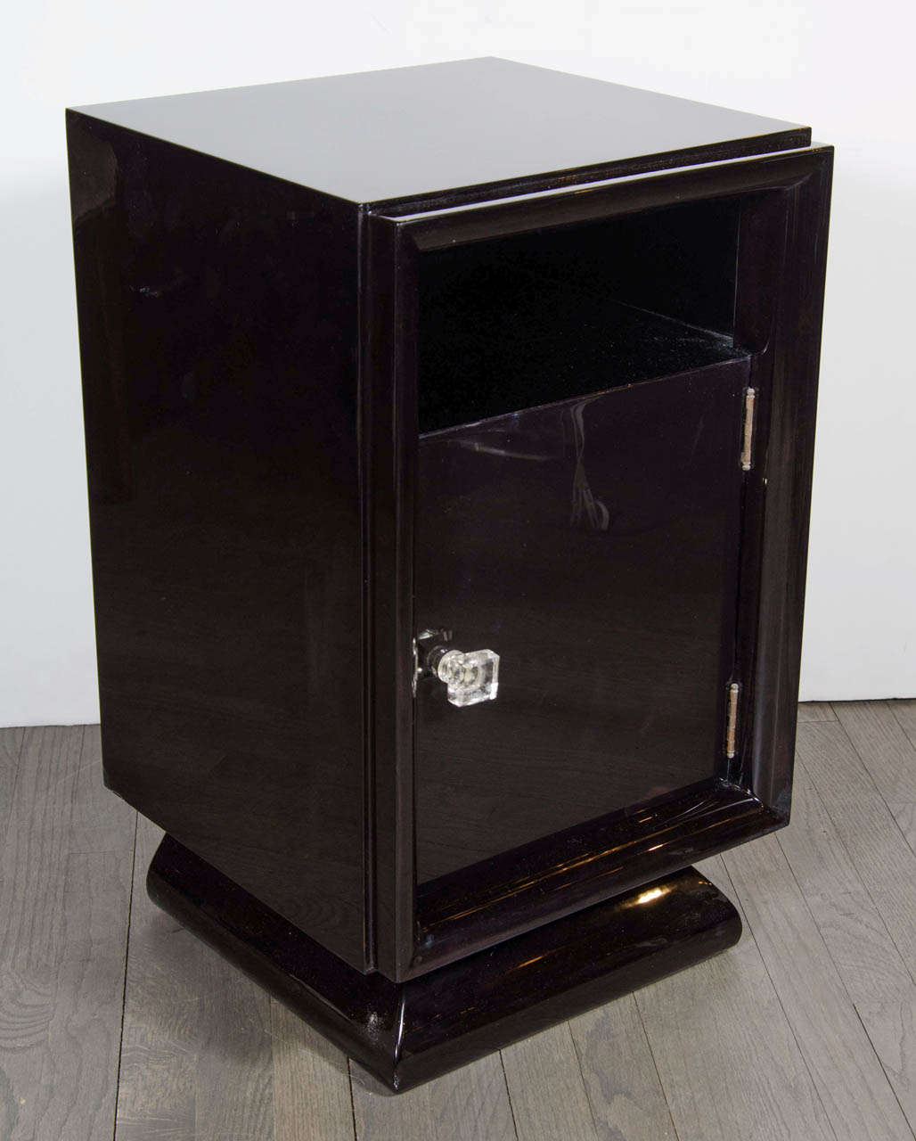 This elegant pair of shadow box nightstands/ end tables were realized in the United States, circa 1950. Realized in beautiful ebonized walnut, they feature a plinth base, a cut out shelf space above a cabinet concealed by a door fitted with a