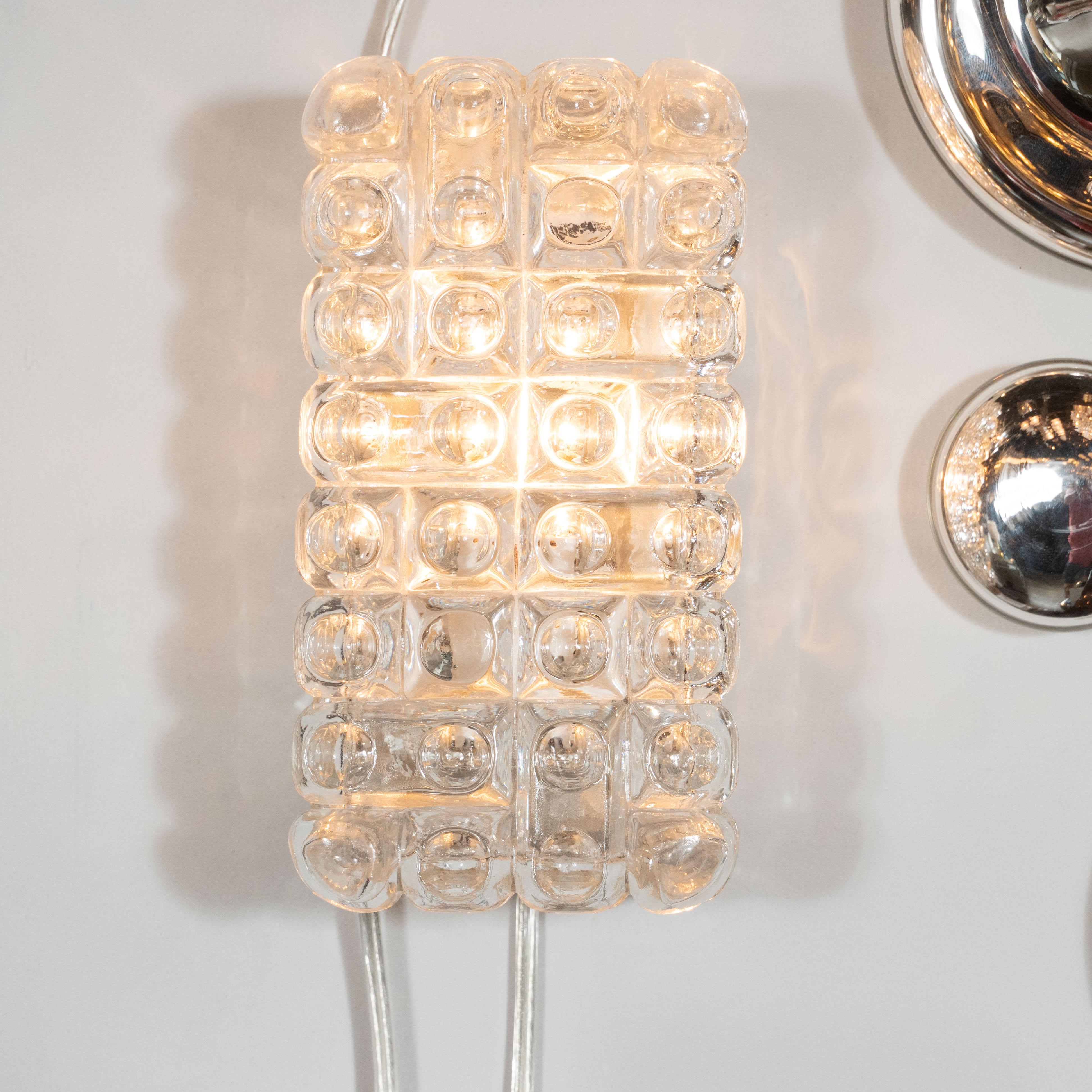 This understated and elegant pair of sconces were realized by the esteemed maker Erco in Germany, circa 1970. They feature rectangular bodies with rounded corners and a lattice pattern formed by intersecting channels etched into the glass. Circular