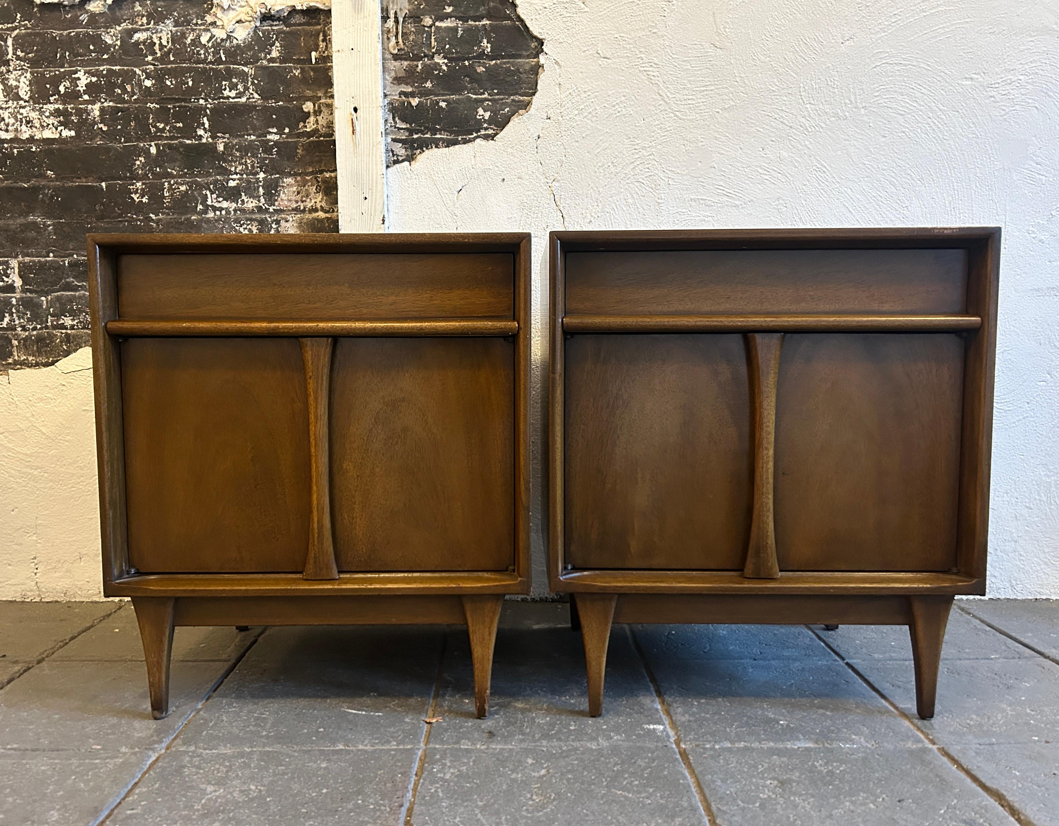 Pair of Mid century Modern American walnut nightstands. Sculpted fronts with a single top drawer and a lower cabinet door on both nightstands. Good vintage condition. Located in Brooklyn NYC

Each nightstand measures 22