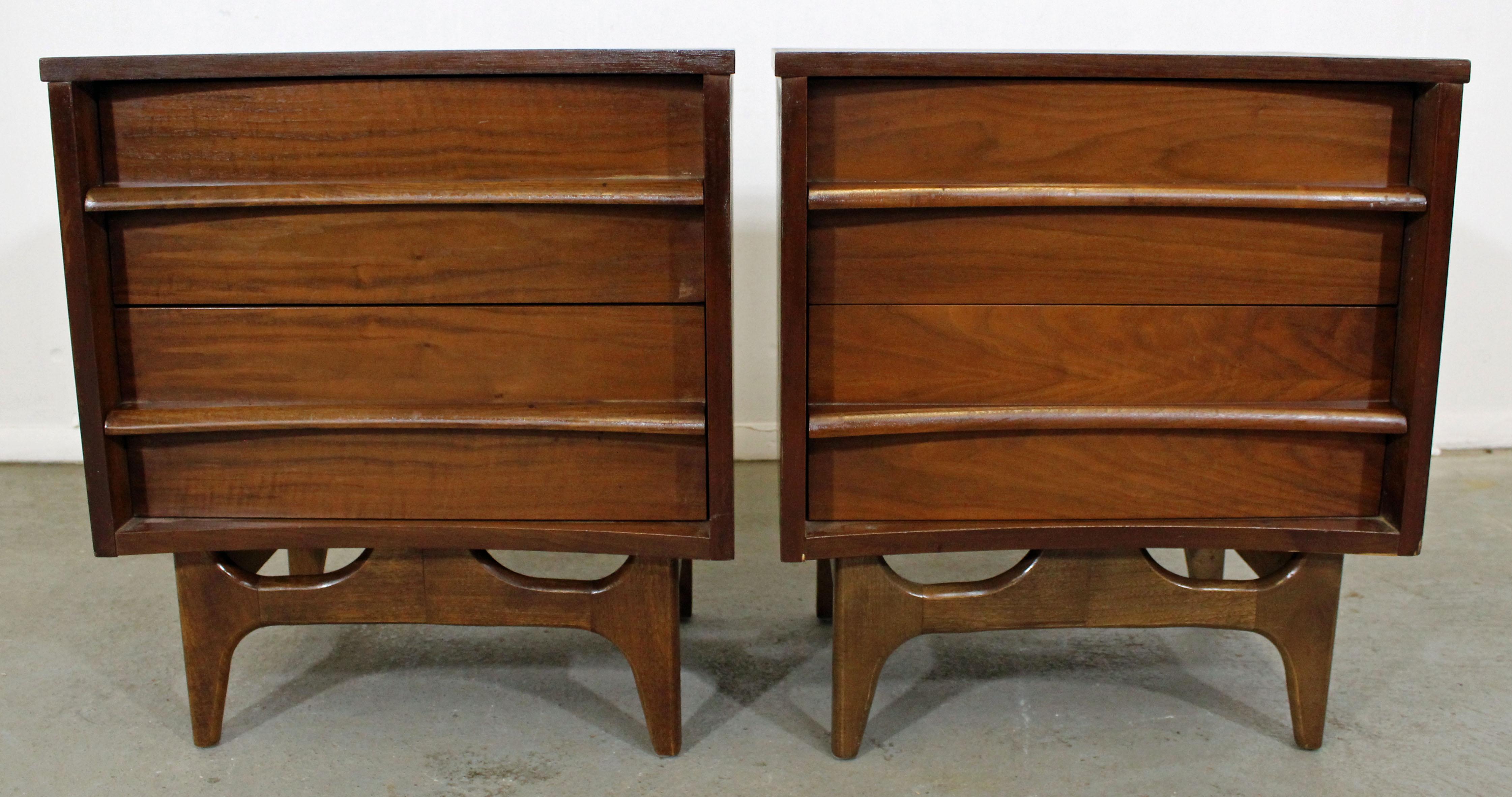 Offered is an excellent example of American Mid-Century Modern design. Includes a pair of walnut nightstands with two dovetailed drawers (each) and sculpted pulls. They are in good condition, show some age wear (refinished tops/sides, some surface