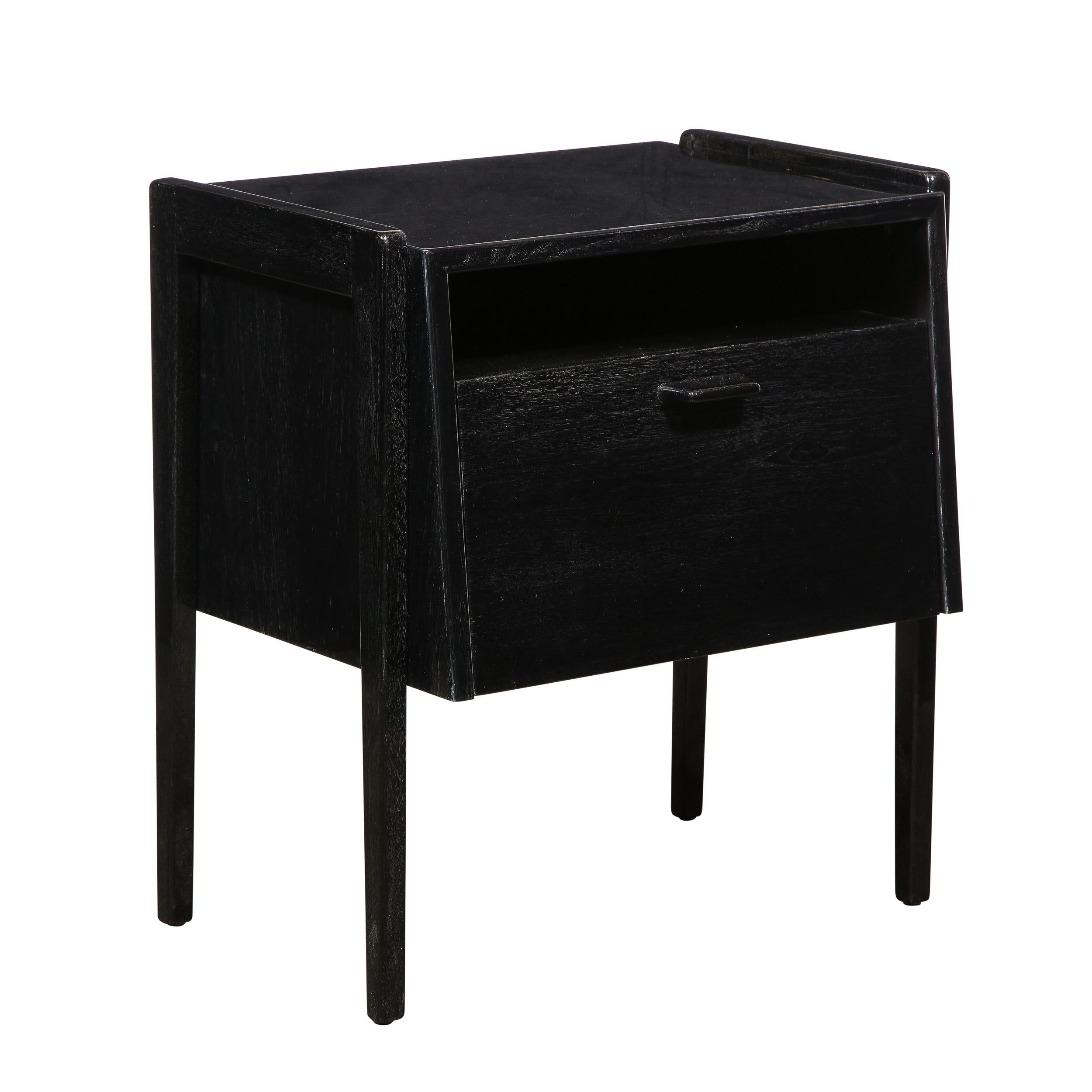 This elegant pair of Mid-Century Modern sculptural nightstands was realized in the United States, circa 1950. They feature volumetric rectangular bodies whose fronts extend on a bias outwards at the base with tapered legs attached to the sides,
