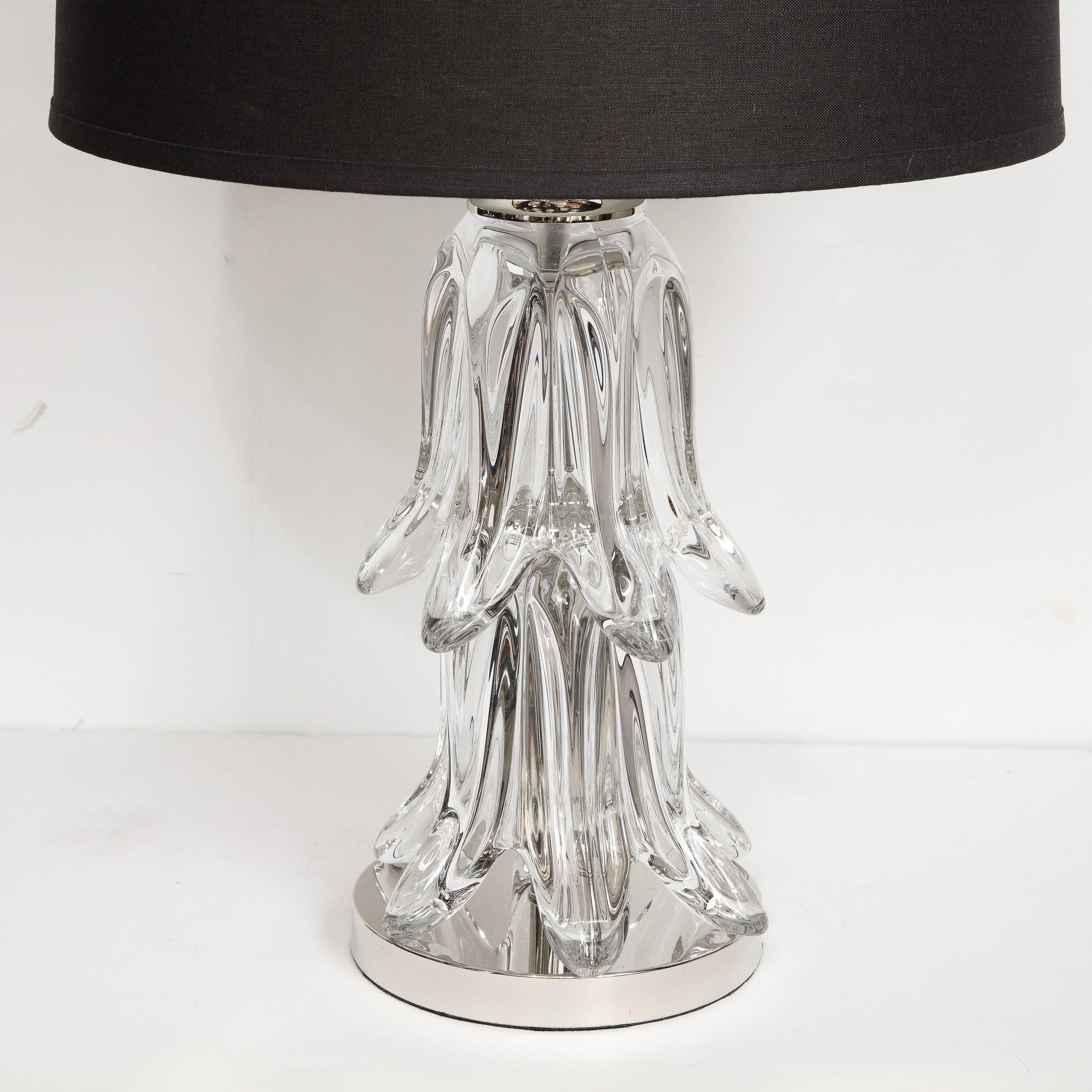 This graphic and refined pair of Mid-Century Modern table lamps were realized in the United States, circa 1950. The lamps feature two tiers of abstracted leaf like forms cascading downwards atop a circular polished chrome base. There are chrome