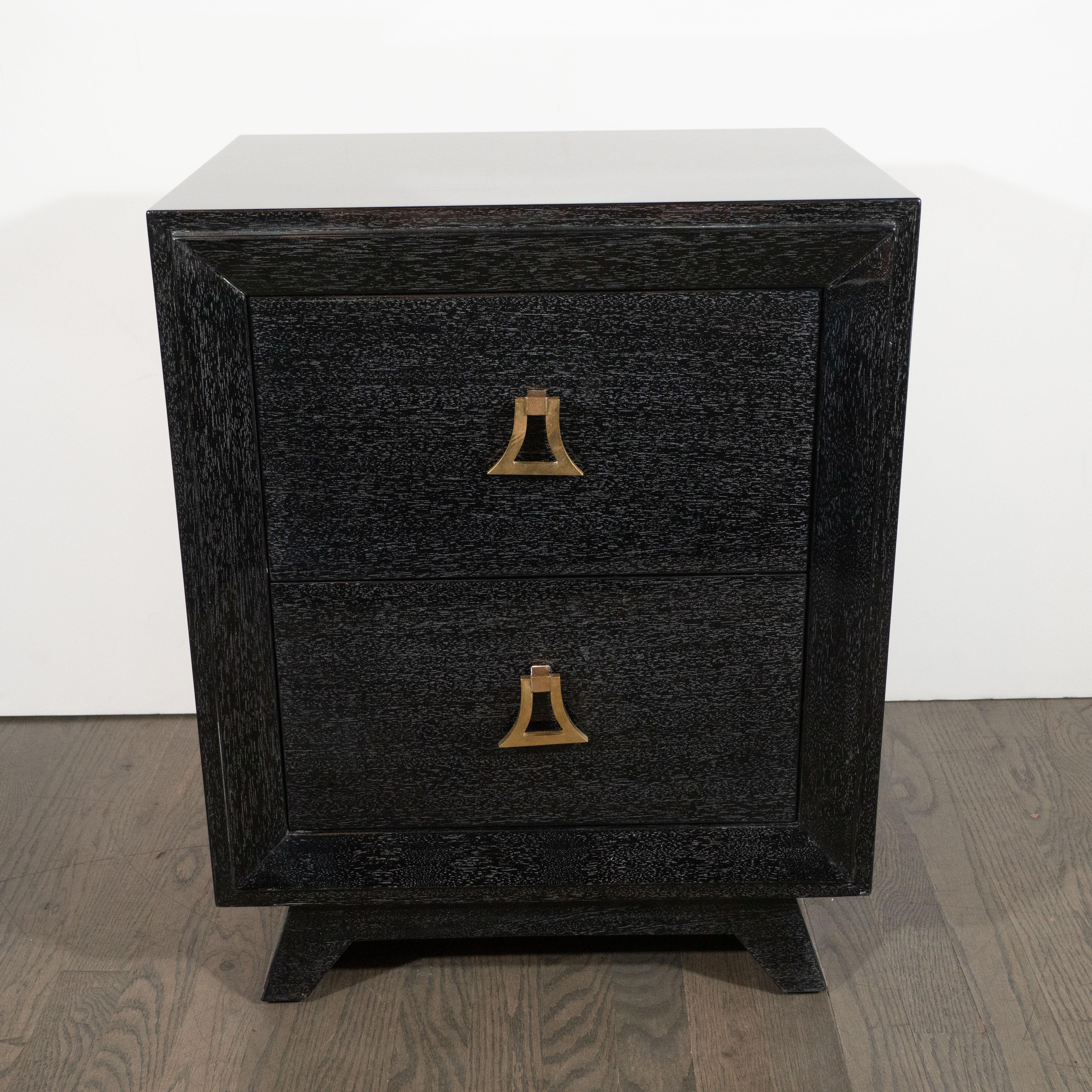 This elegant pair of silver cerused shadowbox mahogany nightstands were realized in the United States, circa 1950. They feature two spacious drawers each fitted with a pair of stylized pagoda style brass pulls. The nightstands sit on rectangular