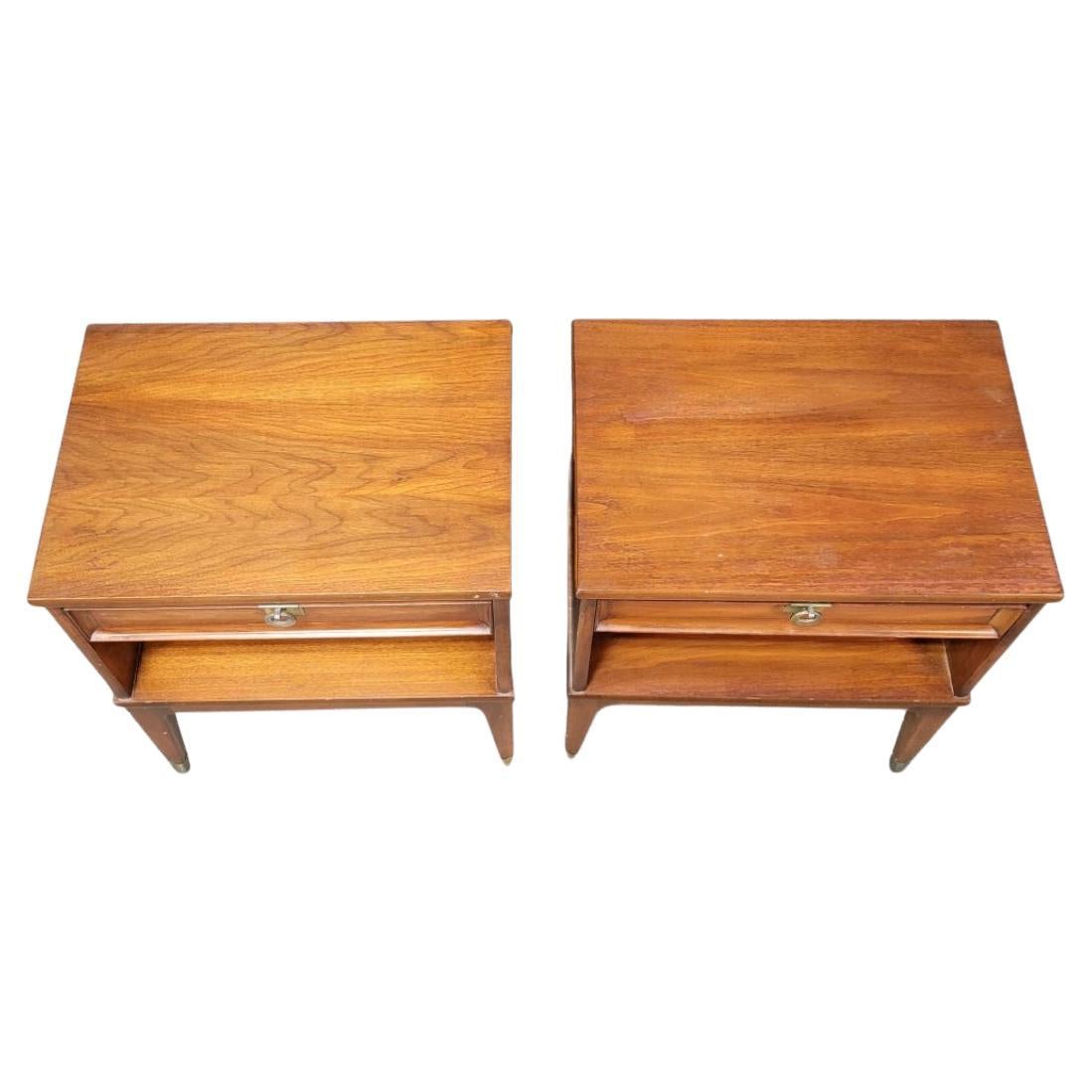 Pair of Mid-Century Modern single drawer Walnut nightstands ring brass handles. Very nice nightstands with 1 drawer each. Each drawer has a hanging brass ring pull. The nightstands are finished in a medium walnut color that sits on a 4 legged wooden