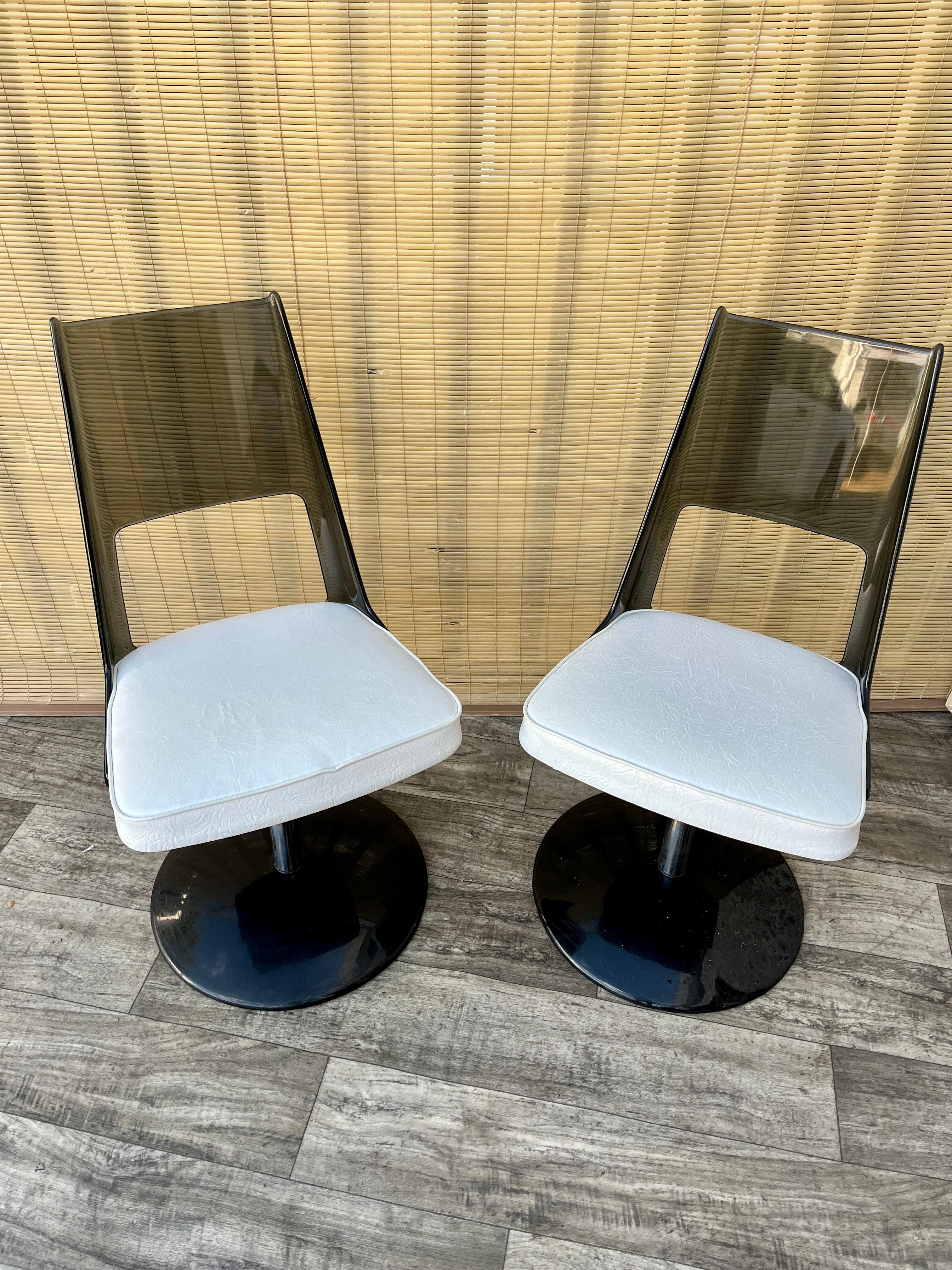 Pareja de sillas de comedor giratorias de lucita ahumada de la colección Mid Century Modern de Daystrom Furniture. Alrededor de 1970
Dispone de respaldos de lucita ahumada con asientos de vinilo blanco, y bases giratorias cromadas y negras. 
En buen