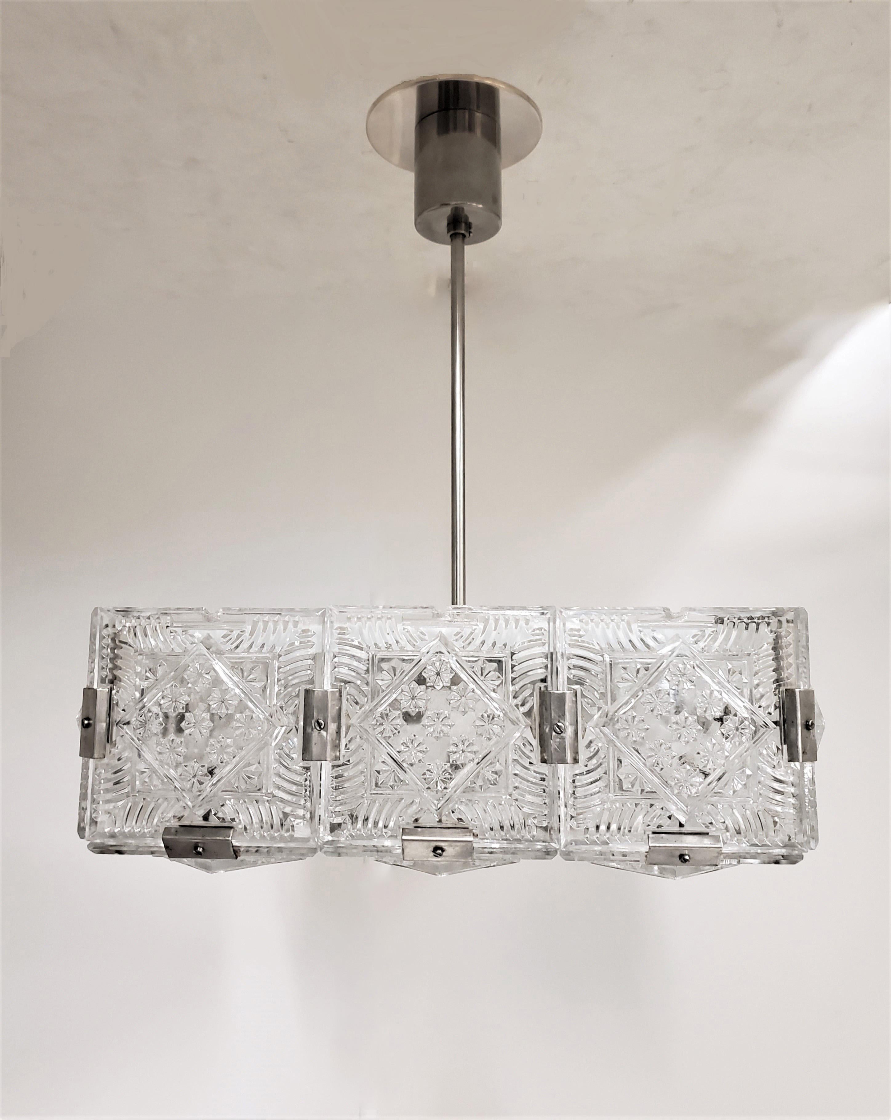 A pair of square Modernist pendant lights comprising small glass elements formed together with original nickeled bronze brackets into a single square unit and supported by a round canopy with rod stem. The juxtaposition of the linear and geometric