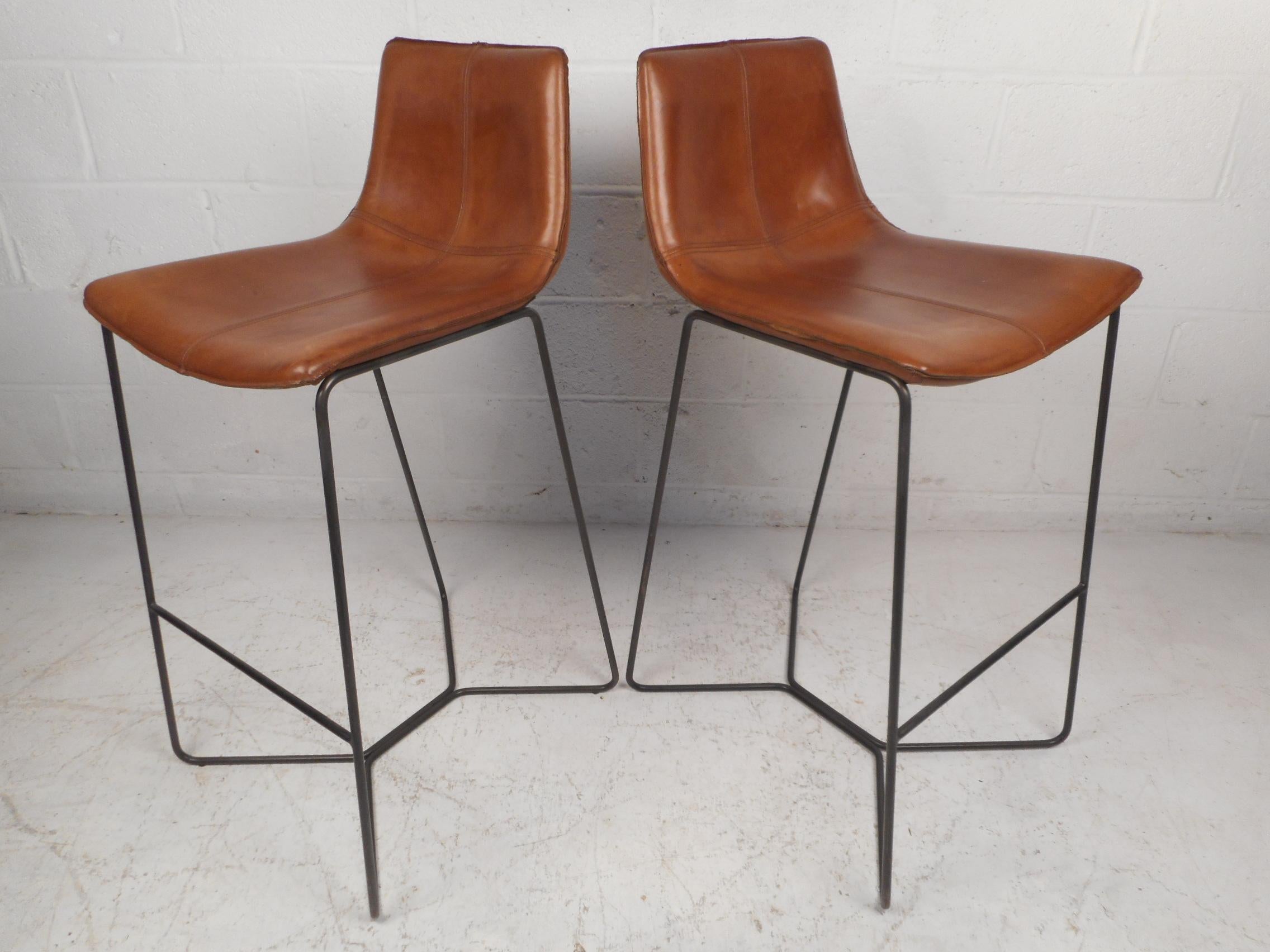 Stylish pair of midcentury high stools with sturdy metal frames and leather upholstery. Form fitting seats along with footrests ensure comfort. This pair would look great situated next to any modern interior's bar or kitchen island. Please confirm