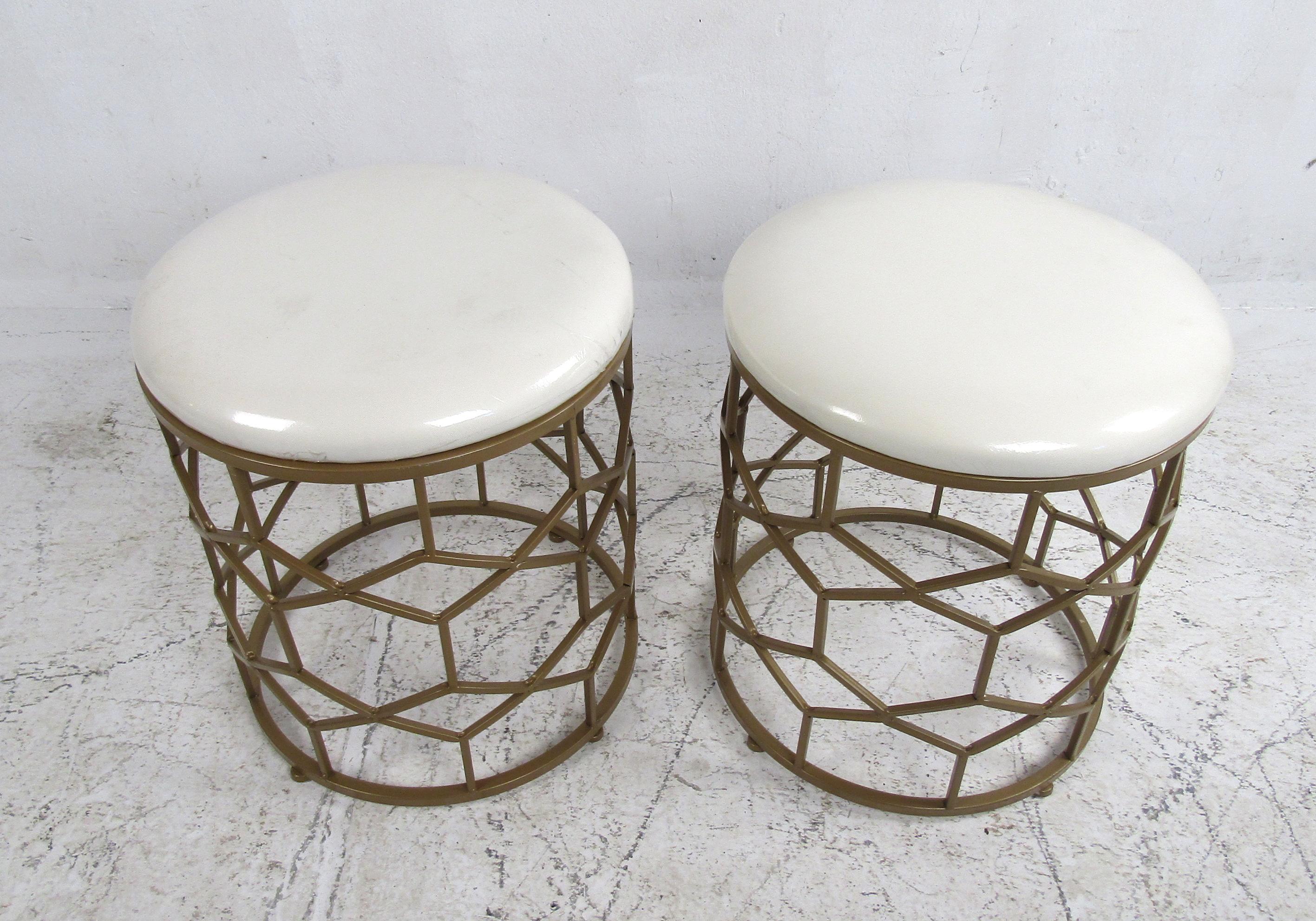 A stunning pair of contemporary modern ottomans boast thick padded tops covered in white vinyl upholstery and unusual faux brass bases. A versatile design that offers comfort without sacrificing style. A lovely circular design that is sure to